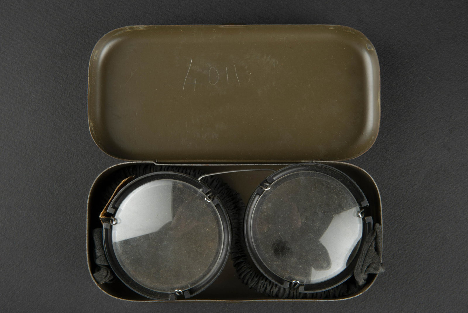 Lunette de vol LW en boite. LW flight glasses in box.: Lunette de vol Luftwaffe en boite. Boite en metal, peinture a 90%. Couvercle bien marque DRP 610809 und 620531. Armature en bakelite et metal, verres blanc. Elastique souple. Reste d etiquette marquee