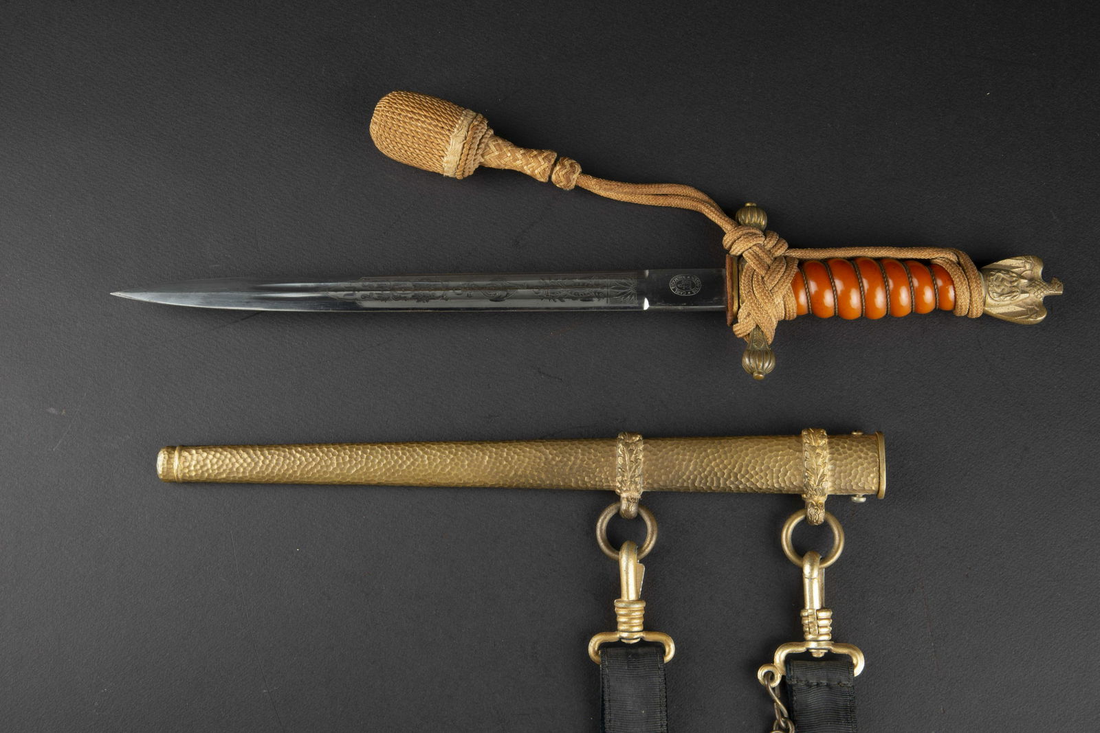 Dague d officier KM. Kriegsmarine dagger: Dague d officier Kriegsmarine. Garnitures en metal dore. Fusee de couleur orange, filigrane present. Dragonne nouee de maniere reglementaire. Fourreau martele, bagues decorees de feuilles de chene. La