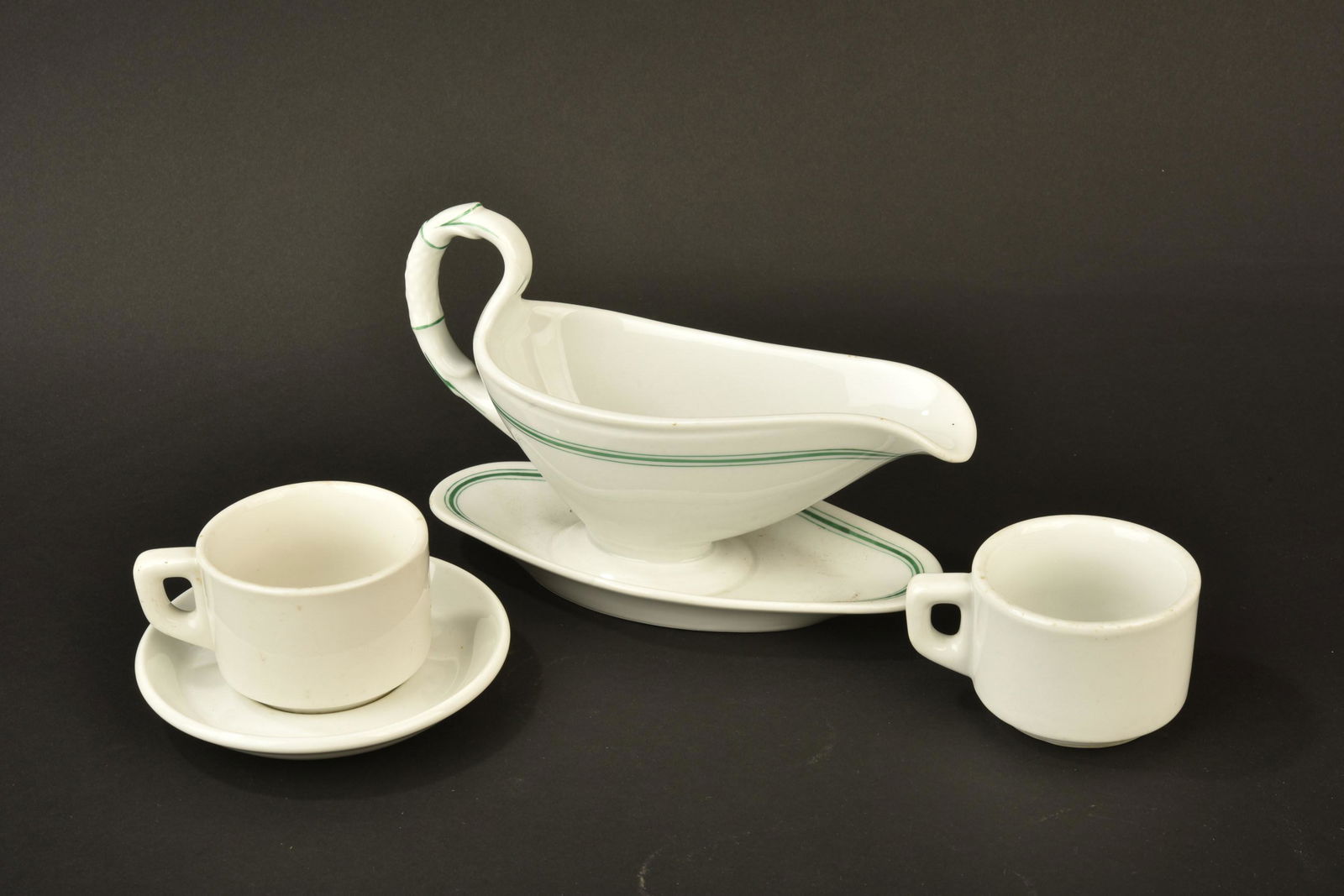 Vaisselle Kriegsmarine. Kriegsmarine tableware: Vaisselle de la Kriegsmarine. Comprenant une sauciere en porcelaine blanche, lisere vert du mess des officiers, bec verseur et anse en parfait etat, longueur 24 cm, fabrication Koenigszelt. Deux tasse