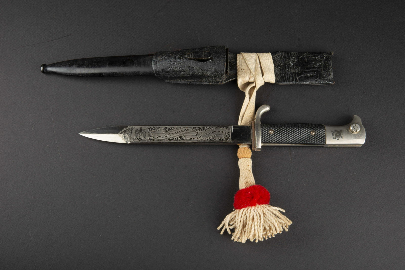 Baionnette de sortie allemande. German exit bayonet.: Baionnette de sortie allemande. Plaquettes en bakelite quadrille. Garnitures metalliques nickelees. Casque allemand et feuilles de chene graves sur le pommeau. Lame dans sa couleur nickelee d origine,