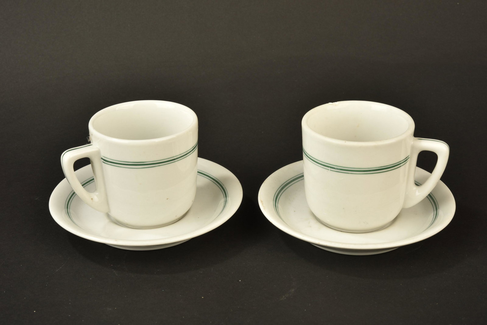 Service a cafe de la Kriegsmarine. Kriegsmarine coffee service.: Service a cafe de la Kriegsmarine. Comprenant deux tasses en porcelaine blanche, lisere vert du mess des officiers, les anses sont completes, un manque sur une bordure, fabrication KMP 1942. Deux souc