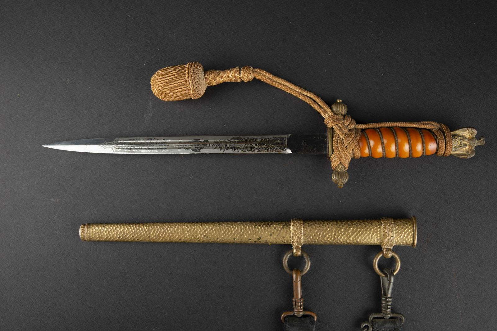Dague officier Kriegsmarine. Kriegsmarine dagger: Dague d officier de la Kriegsmarine. Manche en celluloid orange, filigrane present. Parties metalliques dorees. Dorure a 80% partiellement passee. Dragonne en fil or montee de maniere reglementaire. F