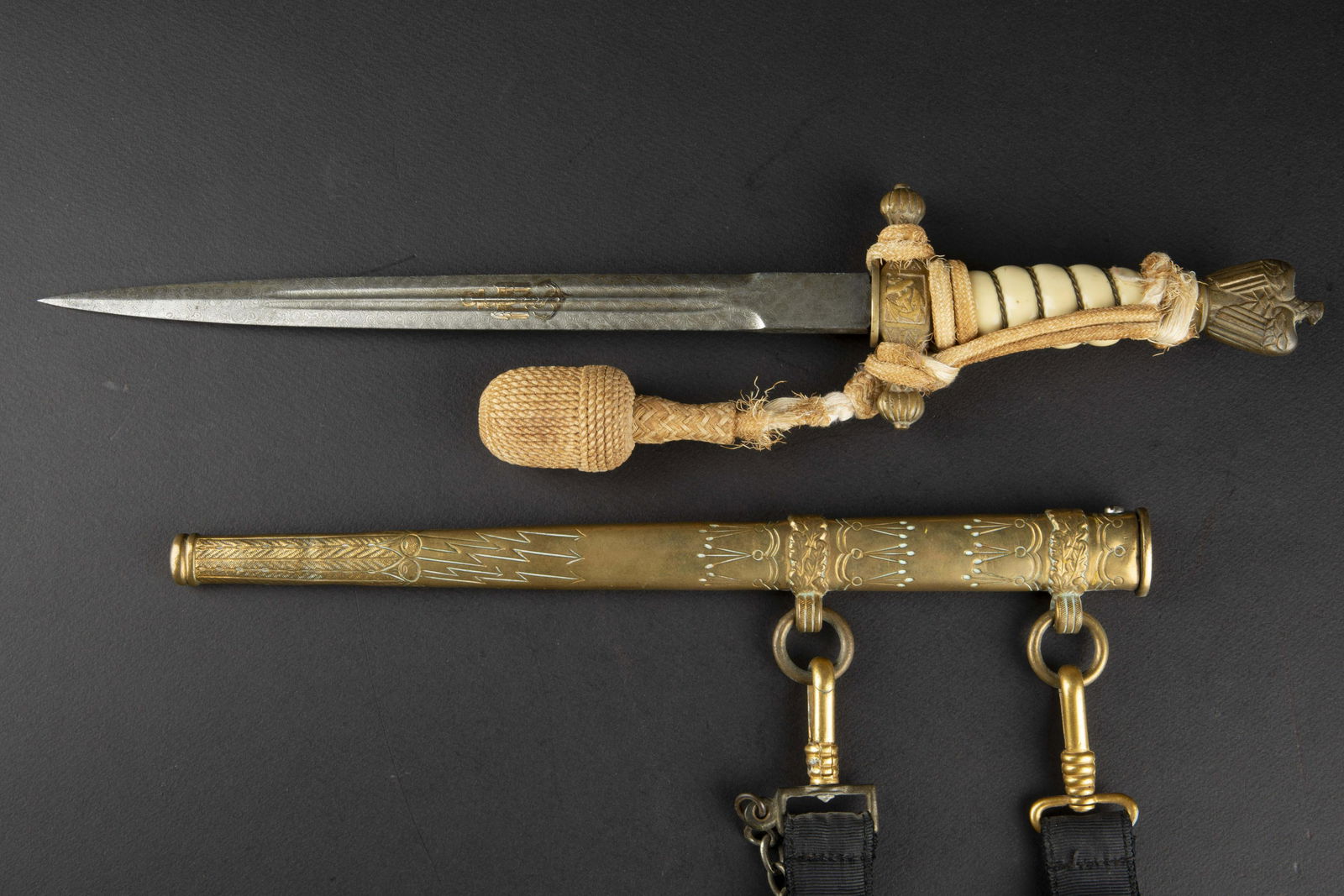 Reproduction dague KM lame damas. Copy Kriegsmarine dagger: Reproduction dague d officier Kriegsmarine lame damas. Belle reproduction des annees 70. Garnitures en metal dore. Fusee de couleur blanche, filigrane present. Dragonne nouee de maniere reglementaire,