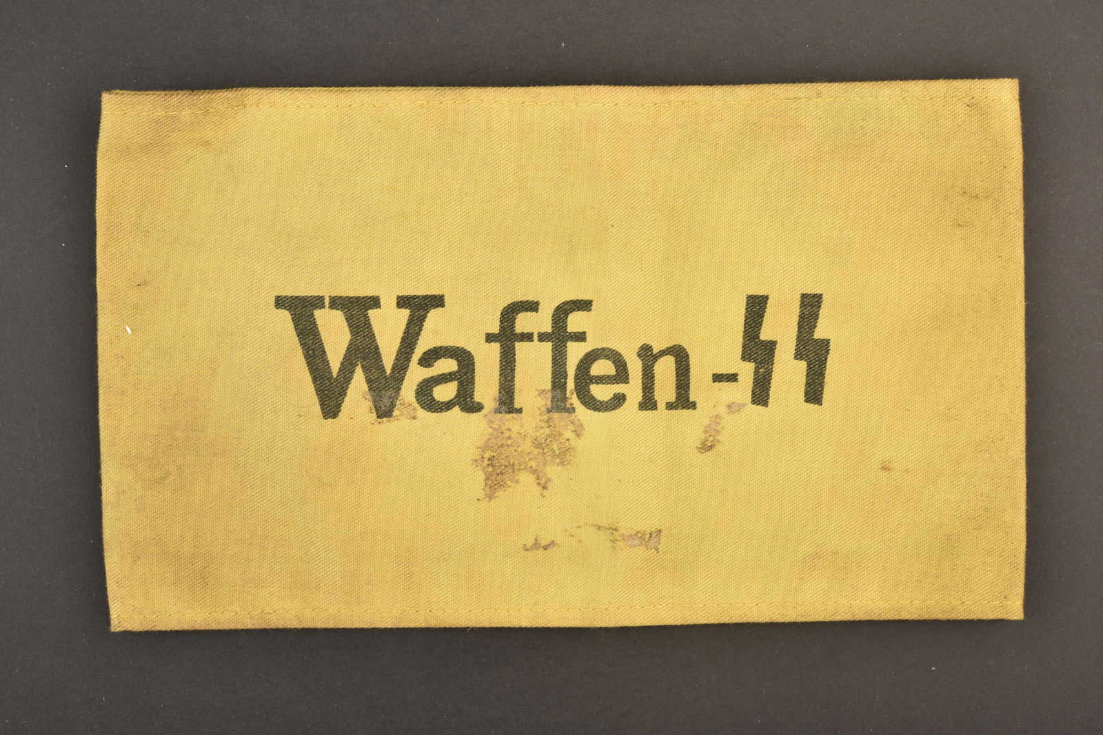 Brassard Waffen SS. SS armband: Brassard Waffen SS. En tissu coton jaune, marquage imprime Waffen SS. Tampons illisibles au dos. A noter une certaine usure et patine de la piece, ainsi que des taches. Etat II+. Waffen SS armband. In