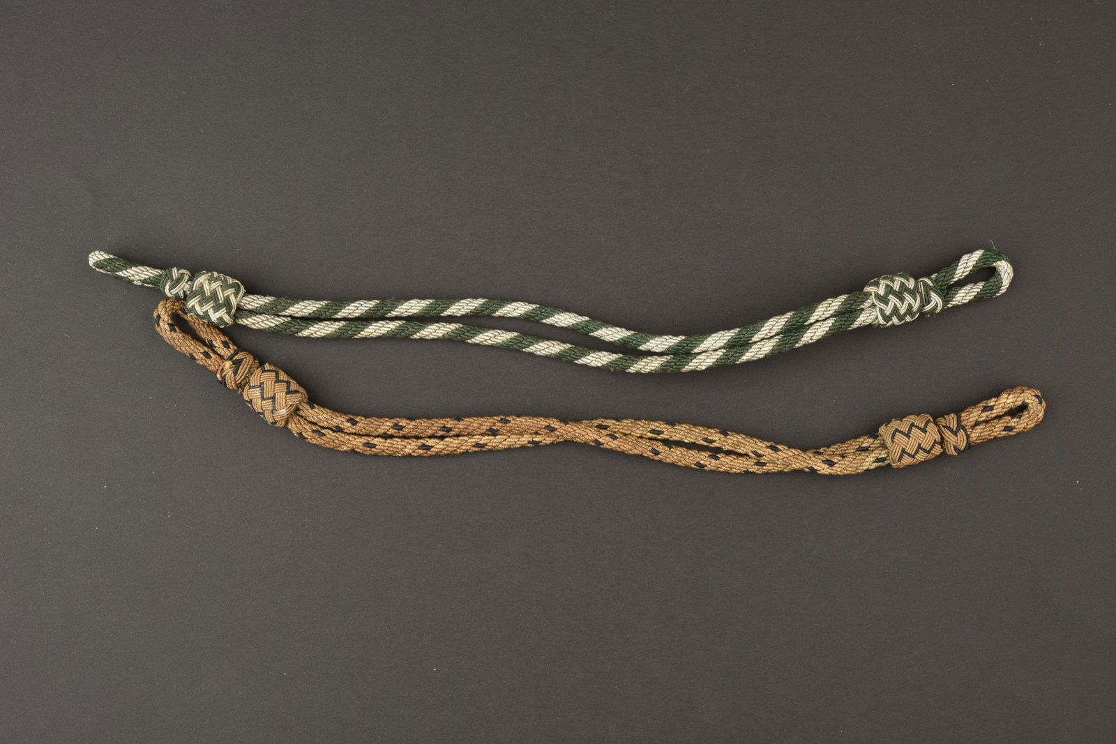 Jugulaires de casquette. Cap chinstraps.: Jugulaires de casquette. Comprenant une jugulaire en fil argent et vert. Une jugulaire en fil or tresse de noir. Completes. A noter une certaine usure et patine des pieces. Etat II+. Cap chinstraps. I