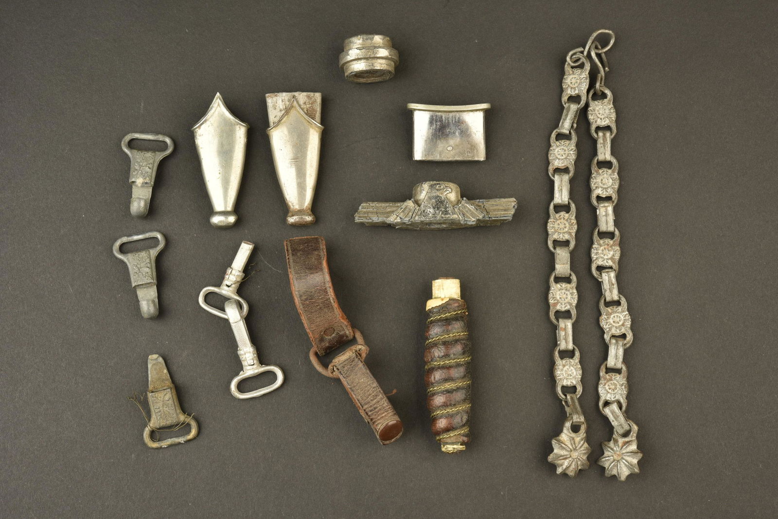 Accessoires de dague. Dagger accessories.: Accessoires de dague. Comprenant cinq mousquetons de belieres, casses. Deux bouterolles de dague. Une fusee en cuir, filigrane present. Un pommeau de dague. Une garde denazifiee. Une entree de fourrea