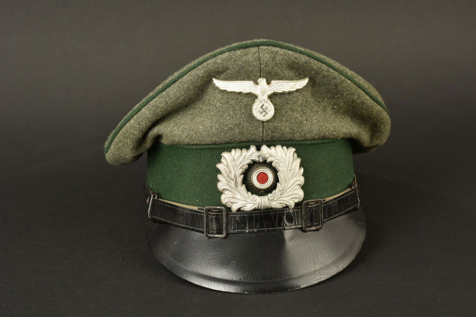 Casquette des douanes. Custom cap: Casquette des douanes. En drap Feldgrau, triple lisere vert des douanes. Insignes en metal. Les insignes n'ont pas ete demontes, afin de verifier les pattes de fixation. Fausse jugulaire en cuir noir.