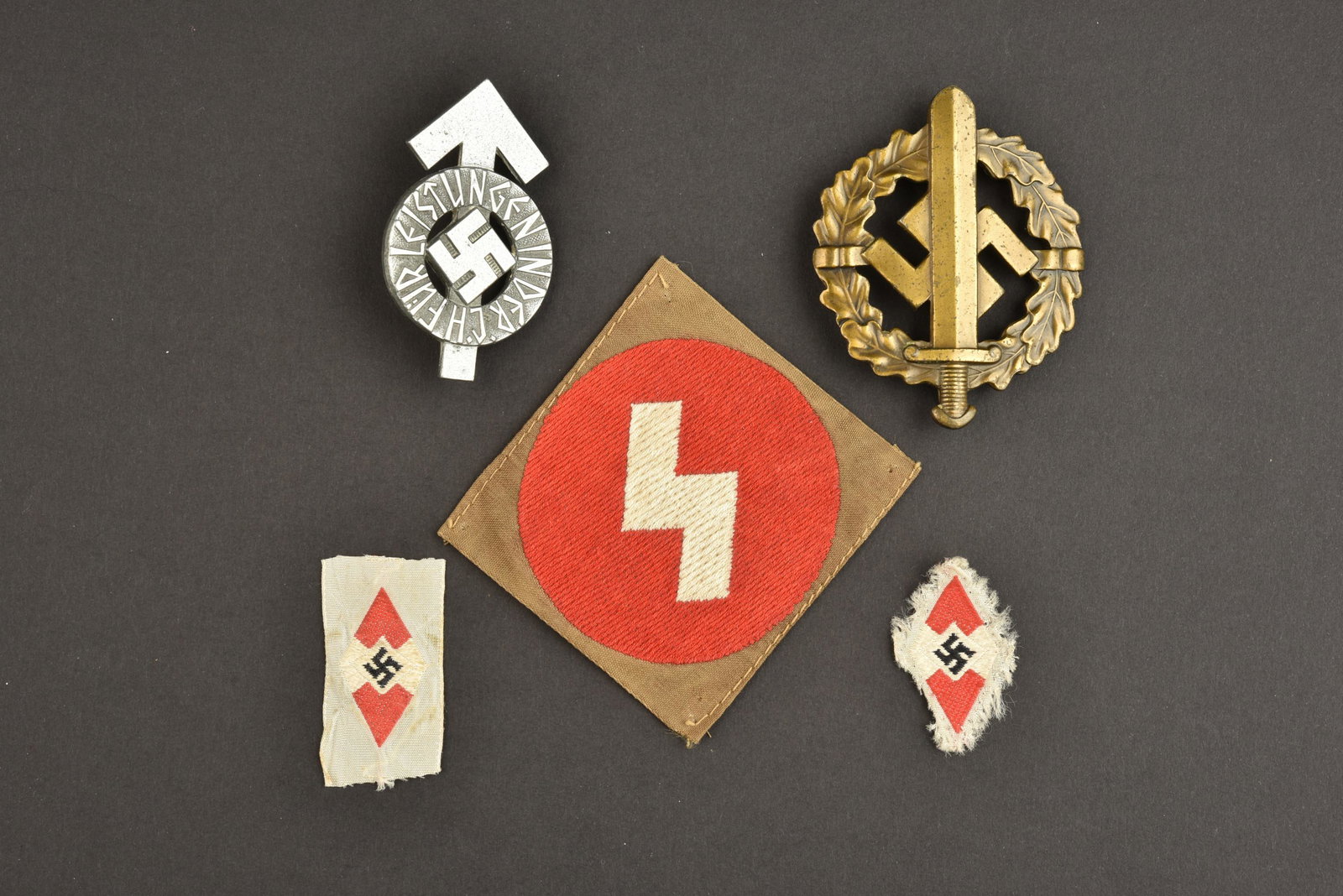 Insignes HJ. Hitlerjugend insignia: Insignes Hitlerjugend. Comprenant un insigne de coiffure tisse, visiblement demonte d'une coiffure. Un insigne HJ tisse, jamais monte. Un insigne de manche HJ, jamais monte, etiquette RZM numero 40856