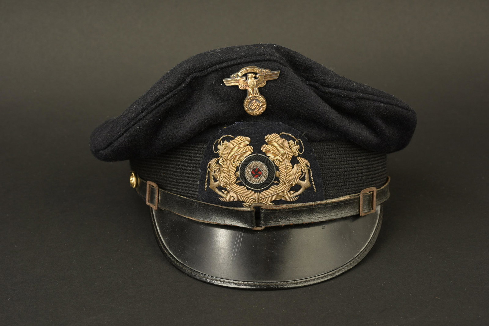 Caquette NSKK Marine. NSKK Navy cap: Casquette NSKK marine. En drap bleu marine. Insigne NSKK en metal dore. Cocardes en cannetille or, montee main. Fausse jugulaire en cuir noir. Les insignes n'ont pas ete demontes, afin de verifier les