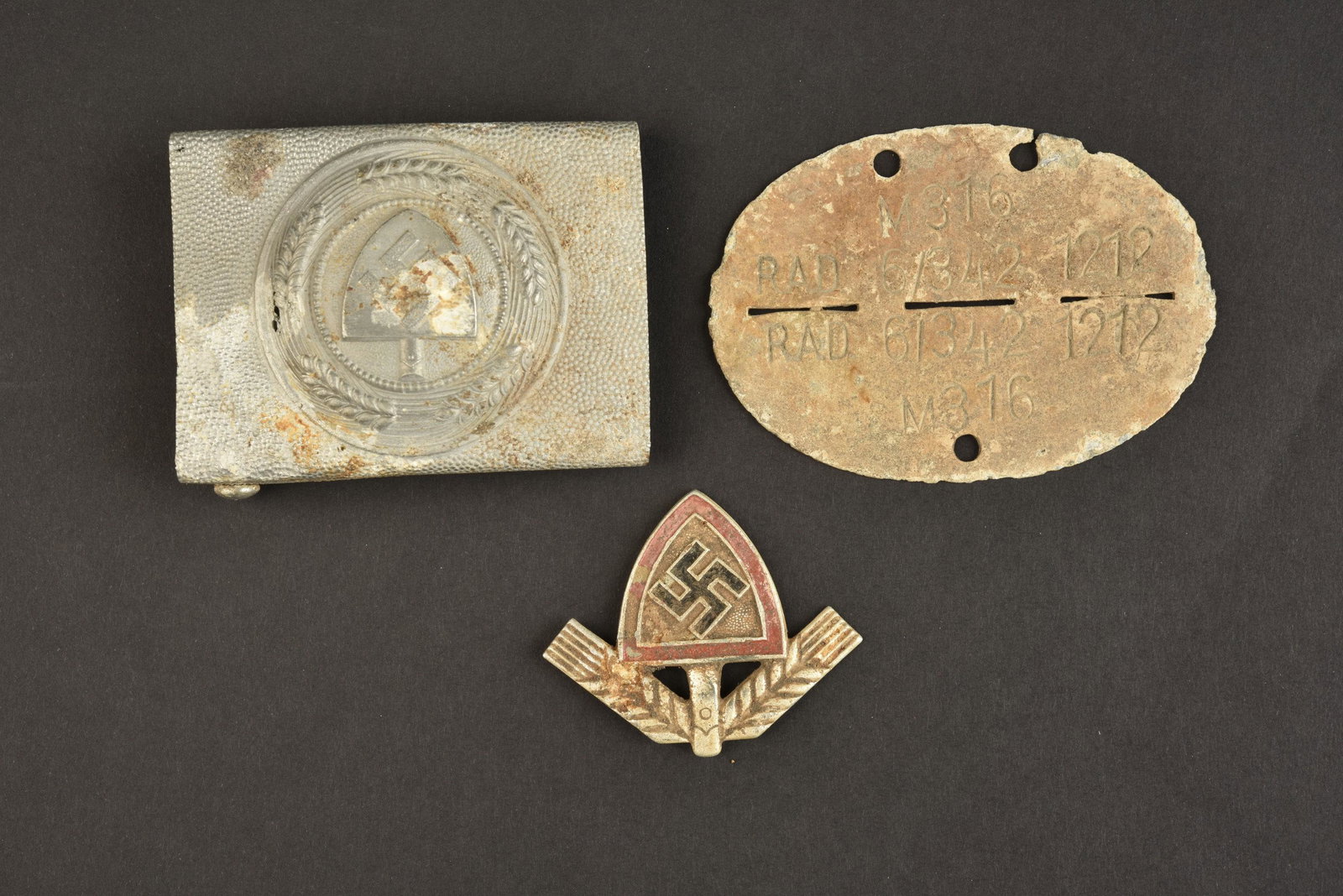 Reliques insignes du RAD Berchtesgaden. Insignia relics of RAD Berchtesgaden.: Reliques d insignes du RAD provenant de l Obersalzberg Berchtesgaden. Comprenant une boucle de ceinturon troupe RAD en aluminium, sans marquages visibles, fortement usee et oxydee. Un insigne de casqu