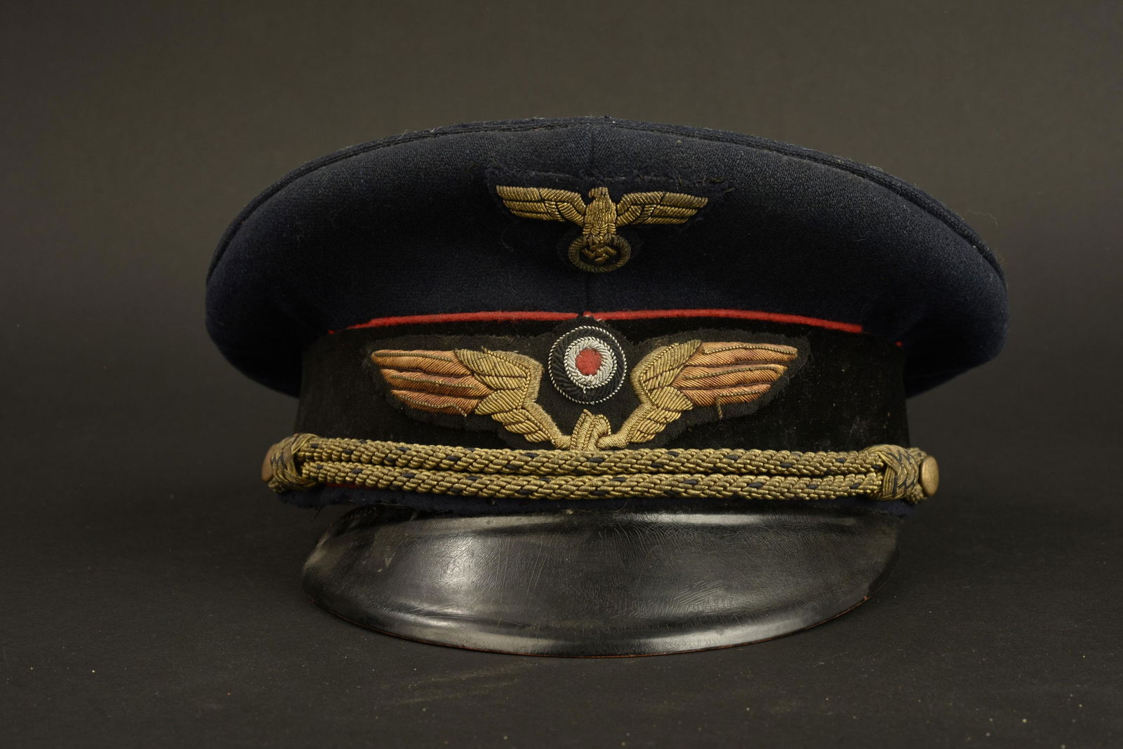 Casquette Reichsbahn. Reichsbahn cap: Casquette Reichsbahn. En drap bleu marine. Triple lisere rouge. Bandeau en drap noir. Insignes en cannetille or. Jugulaire tresse or et bleu. Interieur fortement abime. Bandeau de transpiration decous