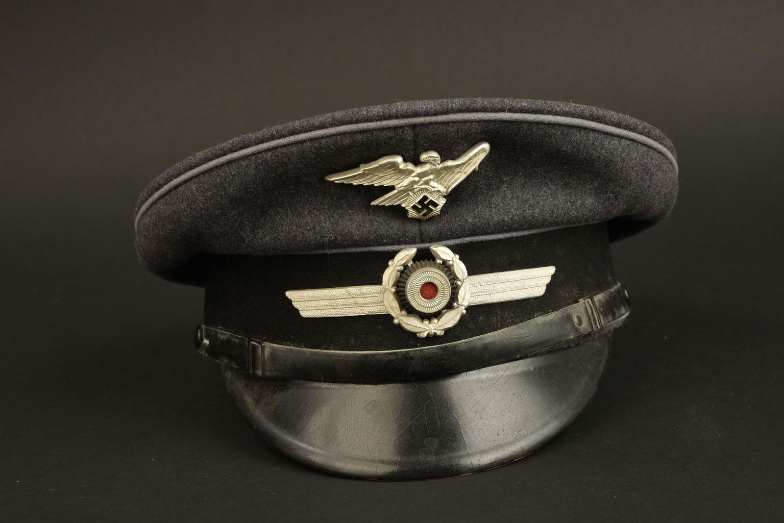 Casquette RLB. RLB cap: Casquette RLB. En drap gris. Triple lisere gris. Insigne RLB du second type. Cocarde en metal. Bandeau en drap noir. Les insignes n'ont pas ete demontes afin de verifier les patte de fixation. Fausse