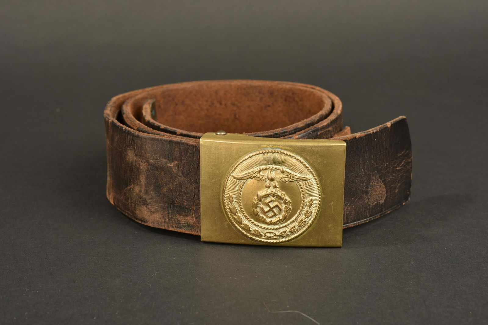 Ceinturon SA. SA belt: Ceinturon SA. Ceinturon en cuir fortement use. Sans marquages visibles. Boucle en laiton dore, sans marquages visibles. A noter une certaine usure et patine de la piece. Etat II+. Belt SA. Heavily wor