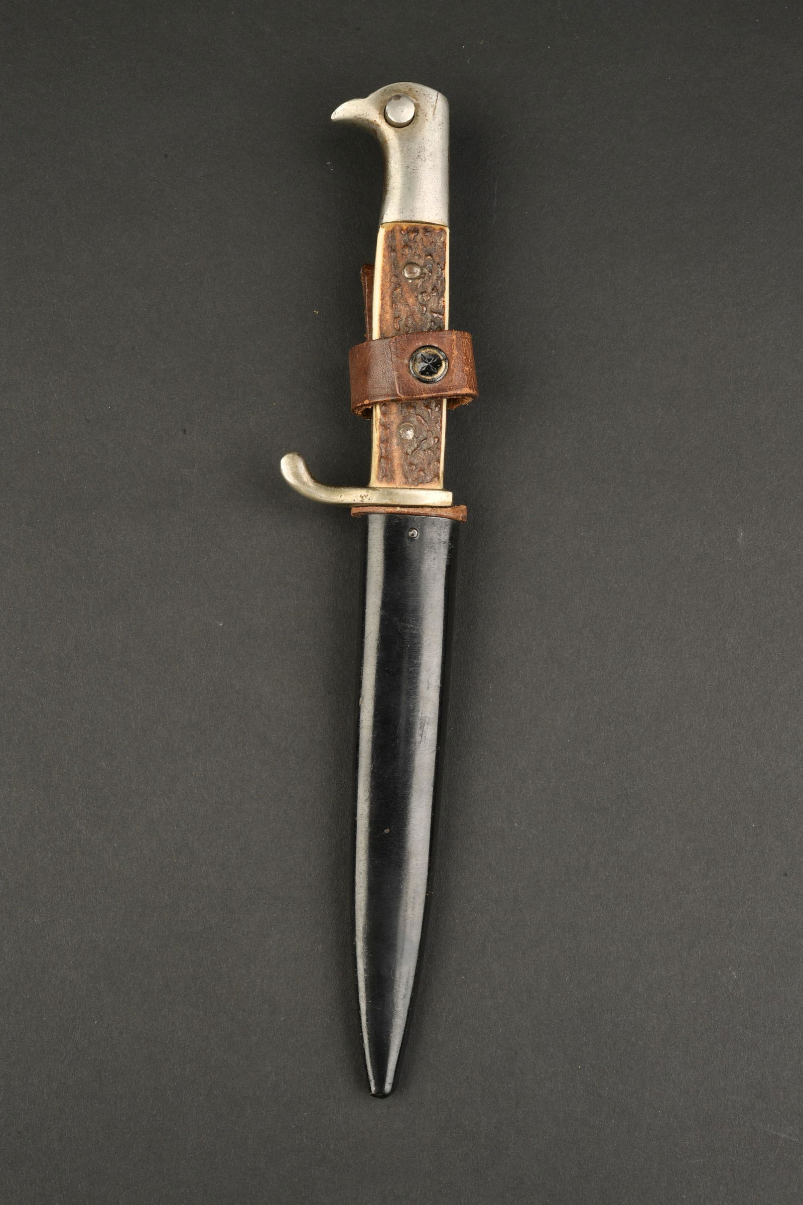 Poignard de tranchee officier. Officer trench dagger: Poignard de tranchee dit d officier avec manche en bois de cerf, pommeau a tete d aigle, lame dans sa longueur d origine. Fourreau en peinture noire avec patte de maintien en cuir fauve, bouton pressi