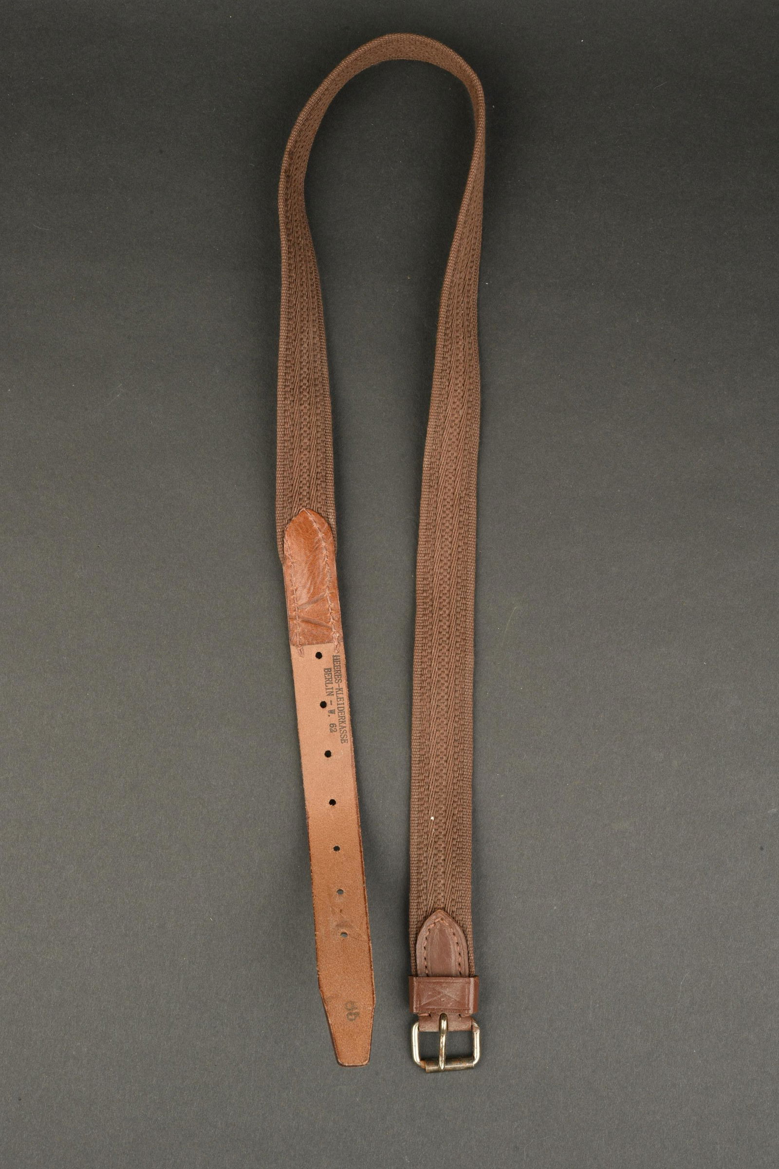 Ceinture allemande. German belt.: Ceinture allemande. En forte toile marron. Cuir fauve. Boucle a un seul ardillon. Marquages Heeres Kleiderkasse Berlin W62. Taille 65. A noter une legere usure et patine de la piece. Etat I-. Plus de