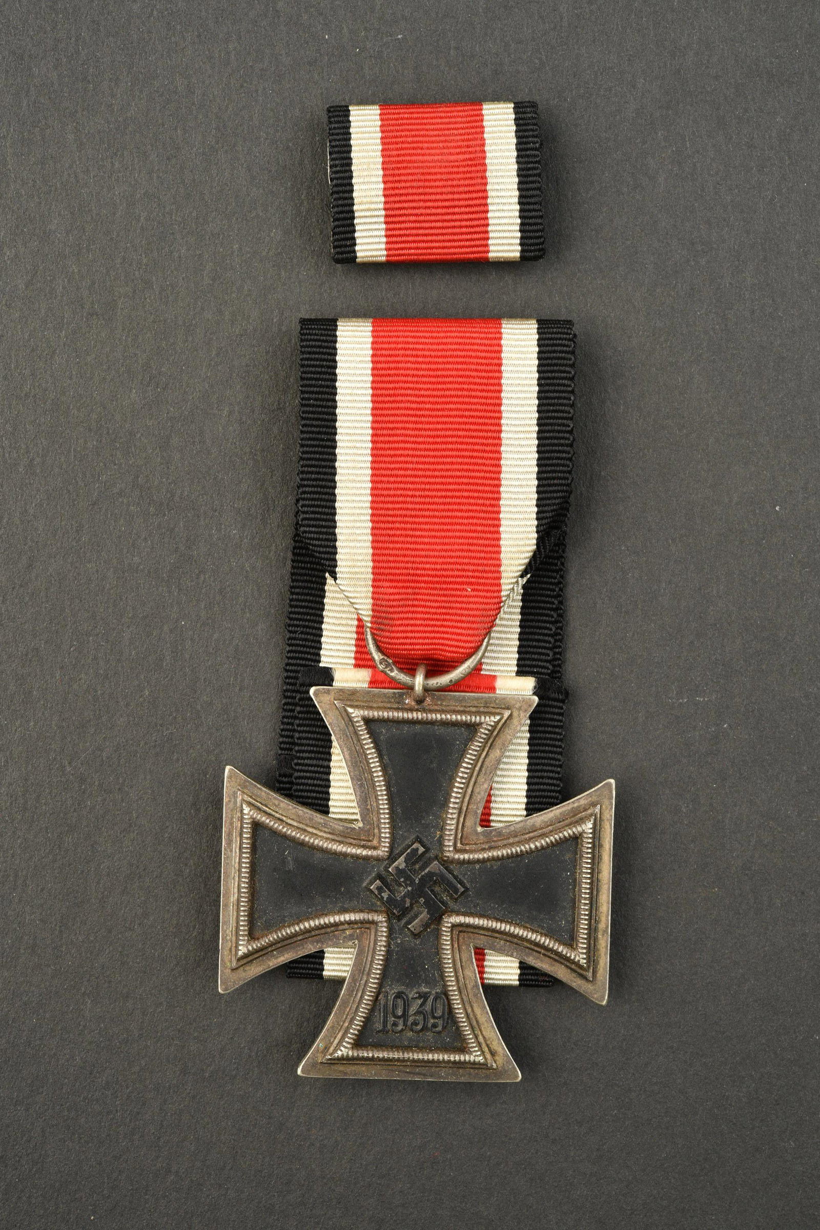 EK II.: Croix de fer de seconde classe. Fabrication en trois parties, peinture noire a 90%. Sans marquages visibles. Ruban complet. On y joint une barrette de rappel de la croix de fer, sur fond en drap Feldg