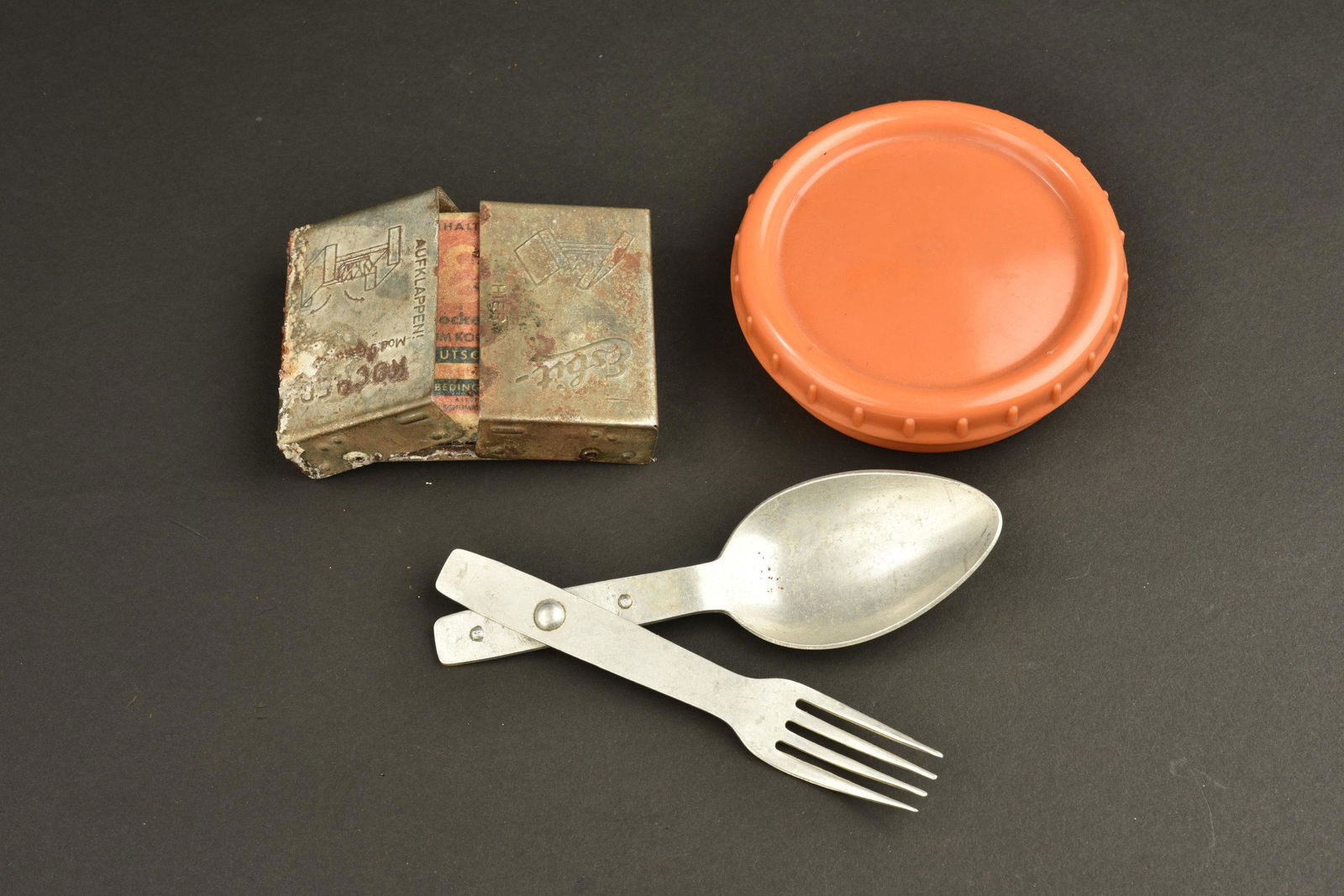 Equipement allemand. German equipment: Equipement allemand. Comprenant un couvert individuel, fabrication CetCW 38. Un rechaud Esbit en metal, fortement oxyde. Une recharge Esbit, complete, emballage abime. Un beurrier en bakelite orange,