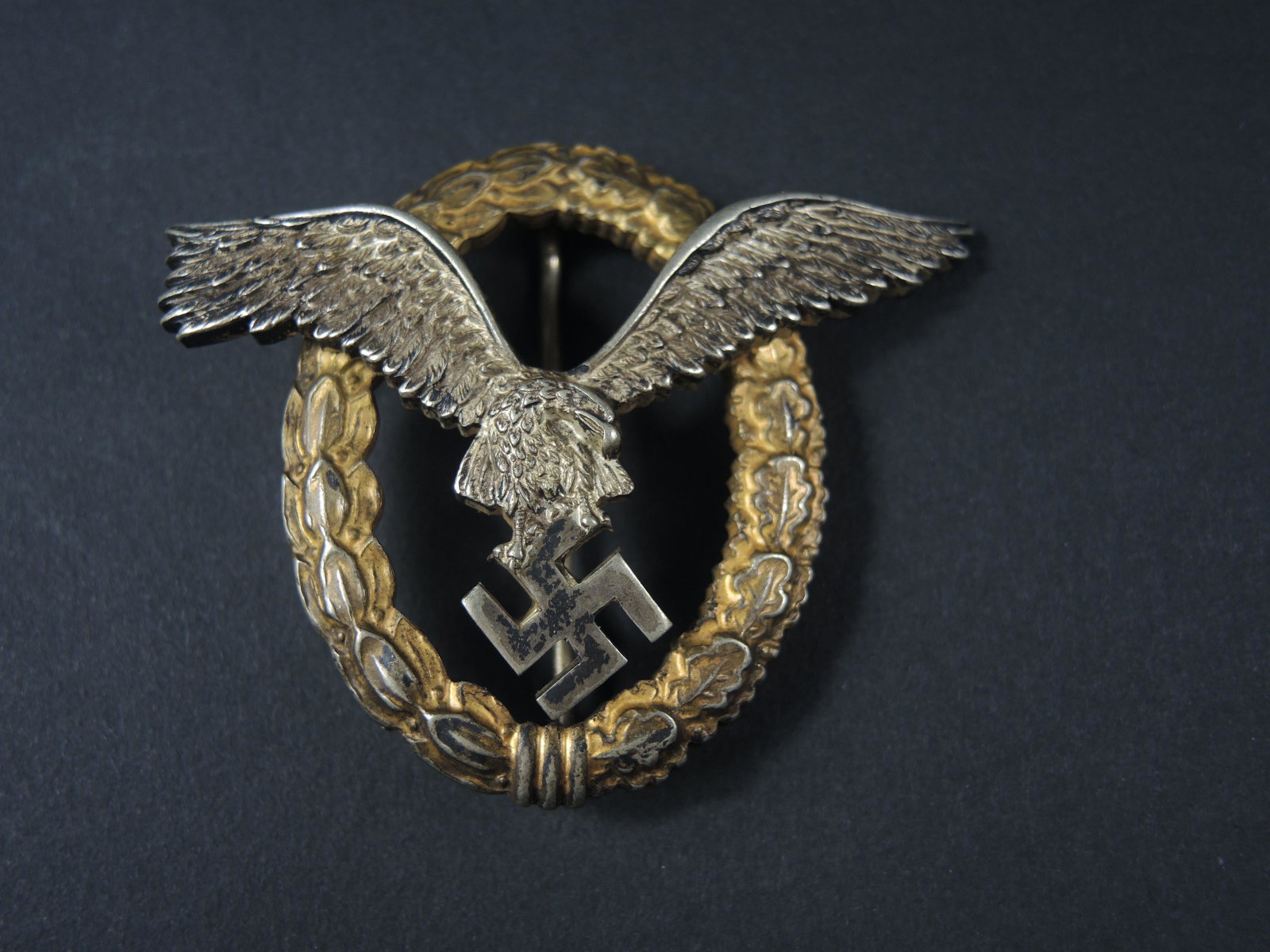 Brevet pilote LW. Luftwaffe pilot s licence.: Brevet de pilote de la Luftwaffe. En m etal, fabrication en deux parties. Aigle pr esentant une couleur argent e a 80%. Couronne de feuille de chene pr esentant une couleur or a 70%. Attache compl ete