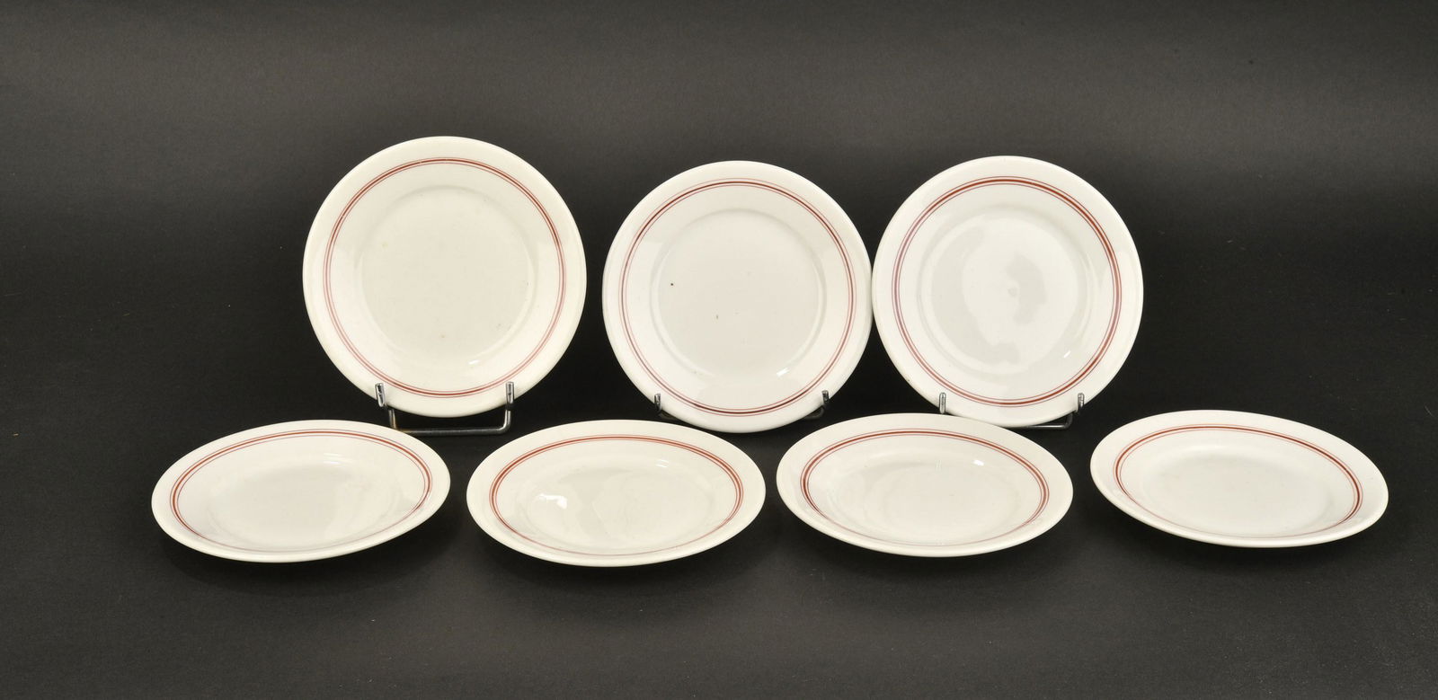 Petites assiettes Kriegsmarine. Small plates Kriegsmarine.: Petites assiettes Kriegsmarine. Sept petites assiettes en porcelaine blanche, liser e rouge. Mod ele pour sous-officier. Fabrication KPM 1941, 1942. Diam etre 16 cm. A noter une certaine usure et pati