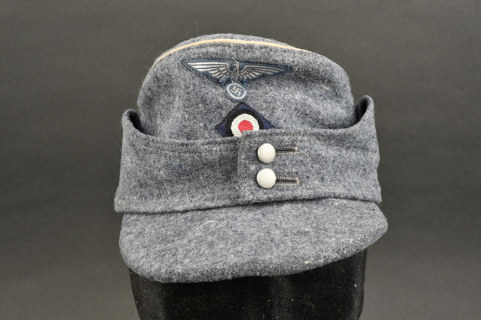 Casquette Bahnschutz. German Banhnschutz cap.: Casquette M-43 Bahnschutz. En drap gris, lisere blanc faisant le tour de la coiffure. Rabat fermant par deux boutons en metal grenele. Insignes Bevo montes machine. Interieur double en satinette bleue