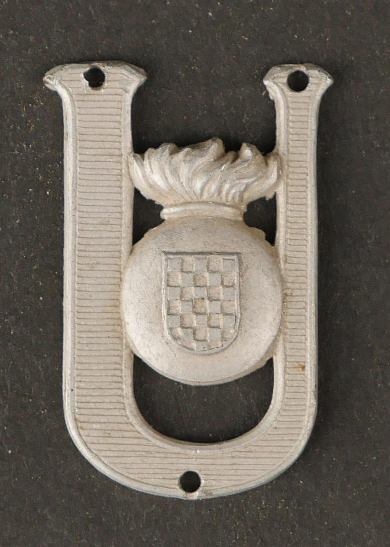 Insigne Oustachis.Ustasha badge.: Insigne de calot Oustachis. En aluminium, trois trous de fixation, sans marquages visibles. Trace de colle au dos. A noter une certaine usure et patine de la piece. Dimensions 2,7 x 1,8 cm. Etat II+.