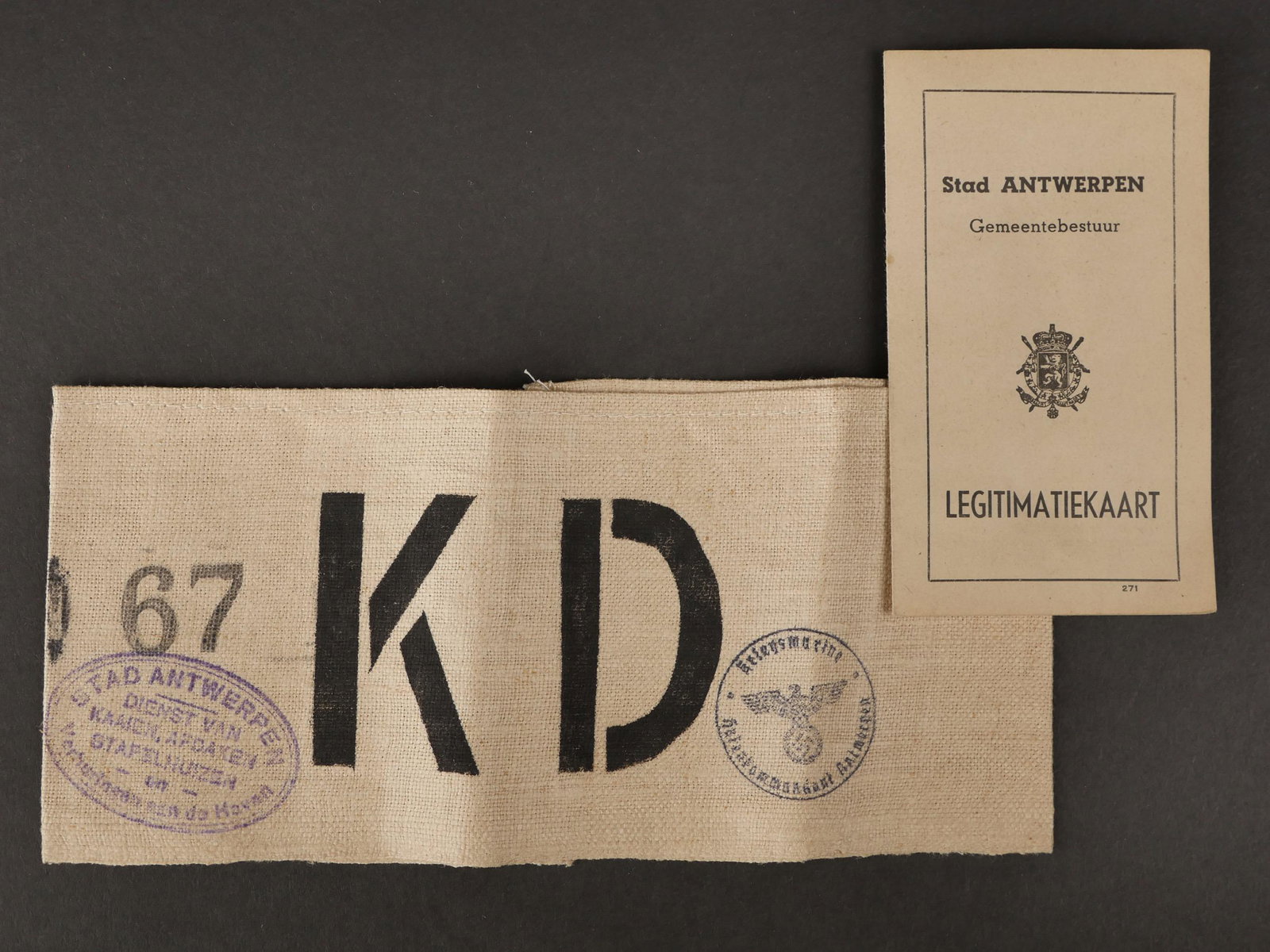 Brassard KD Antwerpen. Armband KD Antwerp.: Brassard KD. En epais tissu blanc. Marque au pochoir noir KD. Tampon marque Kriegsmarine Antwerpen. Stadt Antwerpen Dienst Van Kaaien Afdaken Stafelhuisen. Numero 67. Un petit livret de 4 pages, marqu