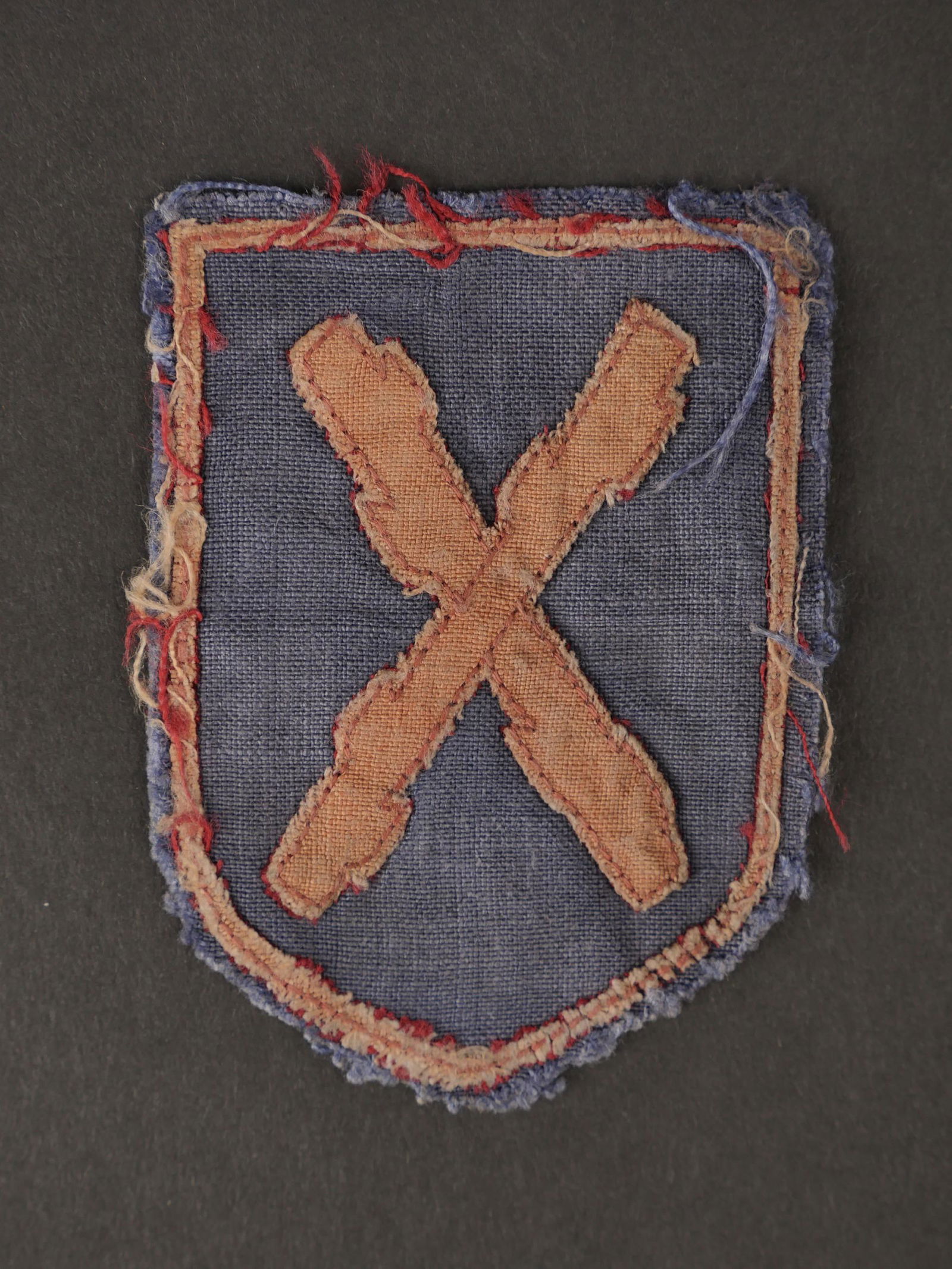 Badge tissu de volontaire rexiste. Badge fabric volunteer rexist.: Badge tissu de volontaire rexiste. Figurant un ecu sur fond gris bleu avec les batons de bourgogne entrecroises rouge au centre et borde dâ€™un lisere de meme teinte. Insigne decousu dâ€™un