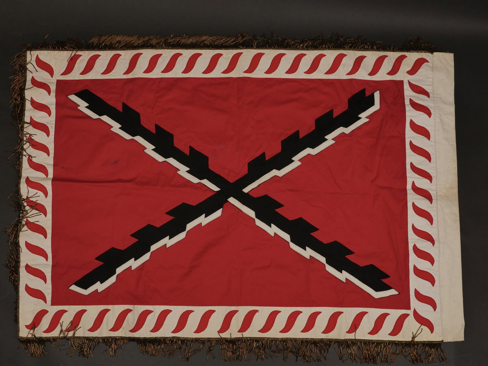 Drapeau presume dâ€™un mouvement Rexiste. Presumed flag of a Rexiste movement.: Drapeau presume dâ€™un mouvement Rexiste. En tissu coton blanc biface representant deux batons de bourgogne noir et blanc entrecroises sur fond rouge, bordure blanche ornee dâ€™une frise de 