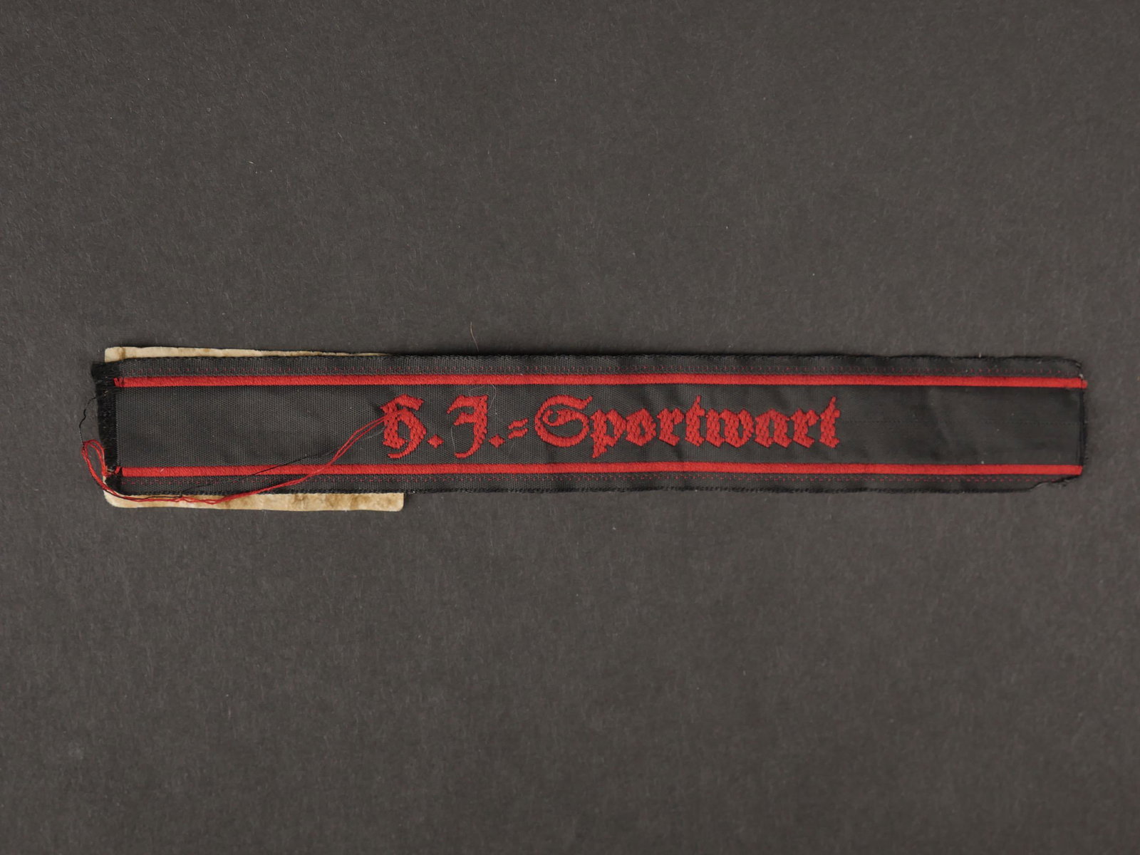HJ Sportwart.: Hitlerjugend Sportwart. En tissu noir, tissage en fil rouge, marque HJ Sportwart. Longueur 14 cm. Jamais monte. Etiquette RZM, numero 053184, code fabricant 241. A noter une legere usure et patine de 