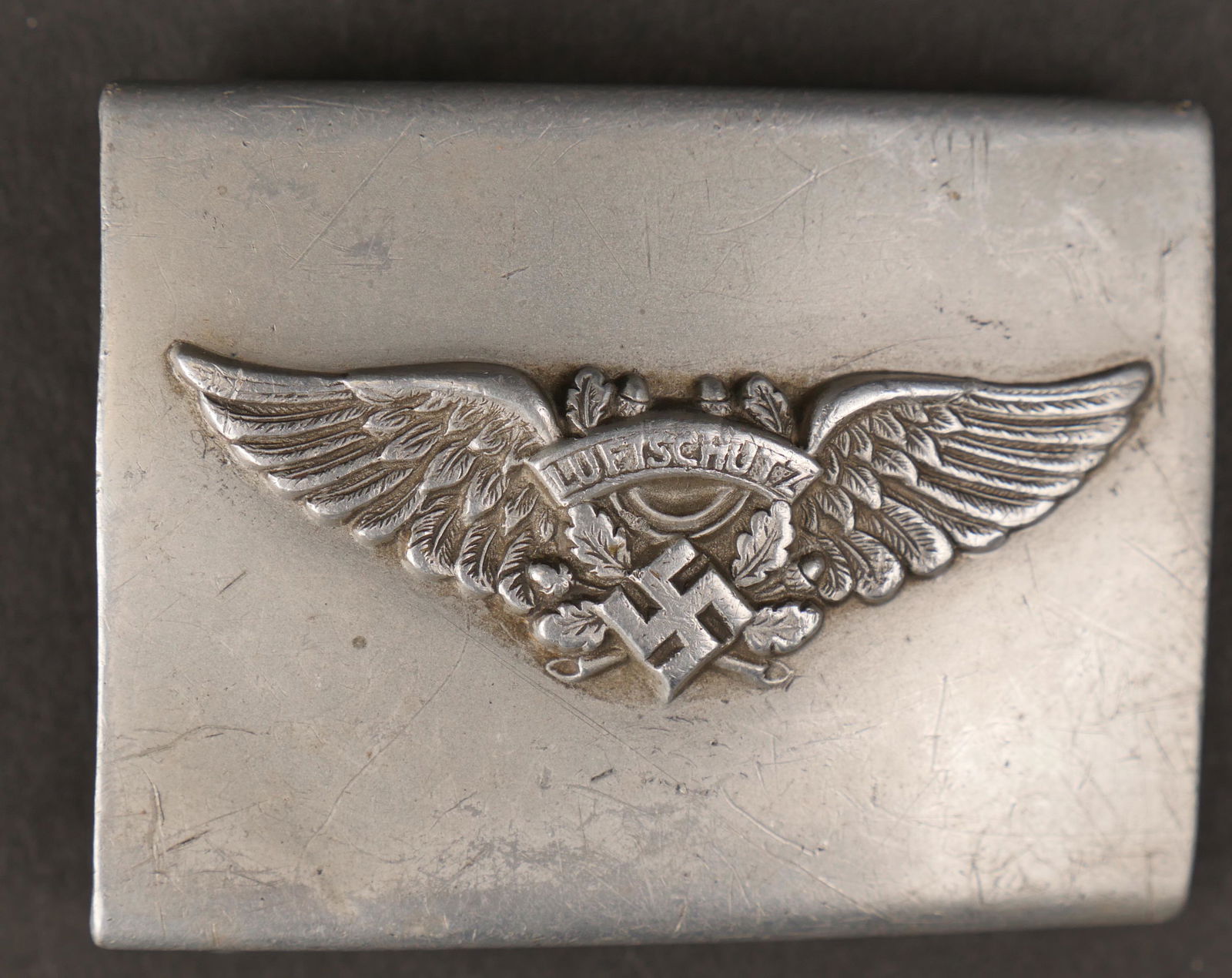 Boucle de ceinturon Luftschutz. Luftschutz belt buckle.: Boucle de ceinturon Lutfschutz. En aluminium, couleur argent. Insigne Luftschutz en relief. Boucle a ardillon complete. Quelques bosses. A noter une certaine usure et patine de la piece. Etat II+. Lut