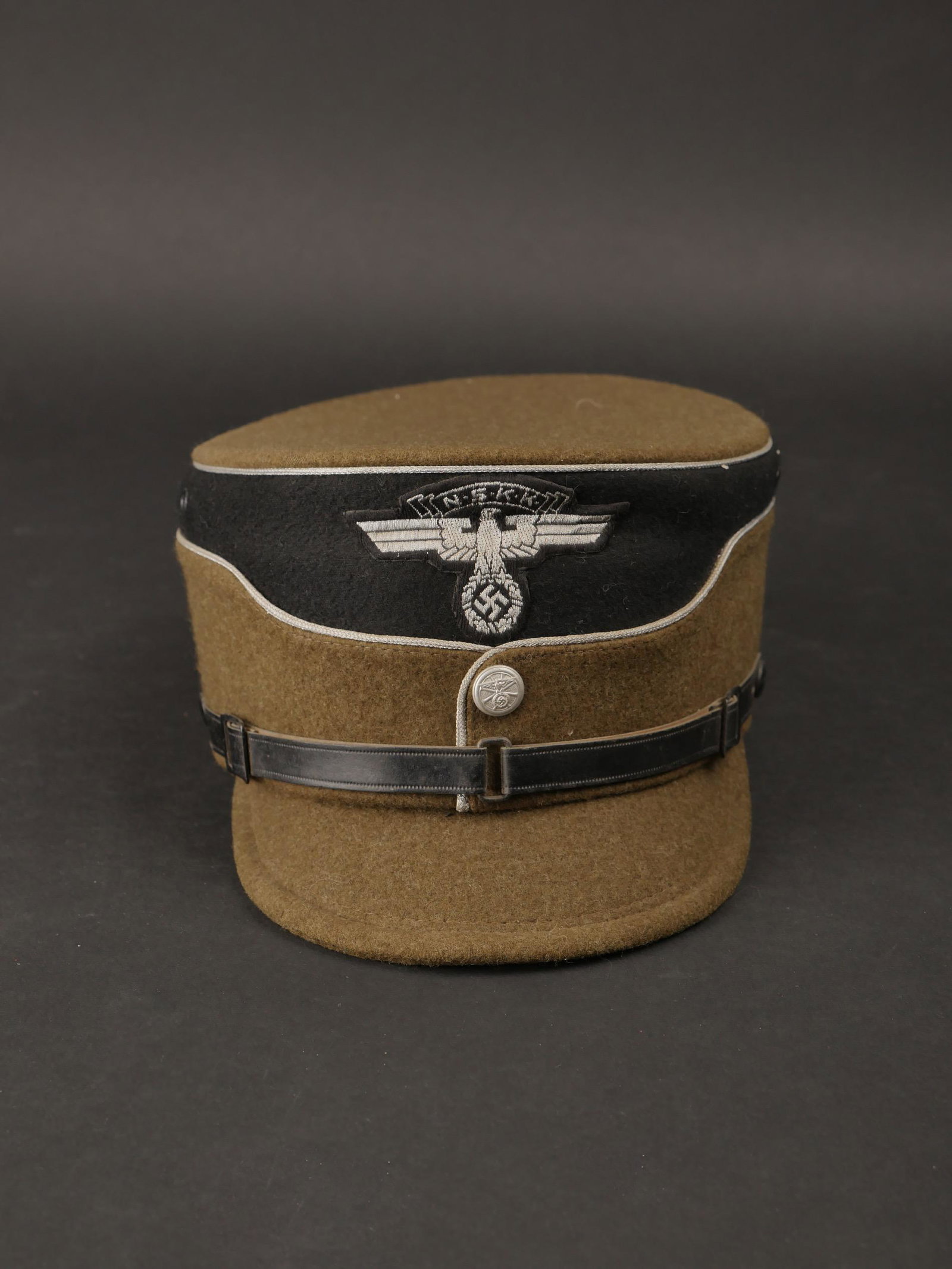 Kepi officier NSKK. NSKK officer kepi.: Kepi d officier NSKK. Modele hivernal en drap kaki. Double lisere argent. Bandeau noir. Insigne NSKK Bevo monte main. Bouton en aluminium disposant de l insigne du NSKK. Fausse jugulaire complete. Vis