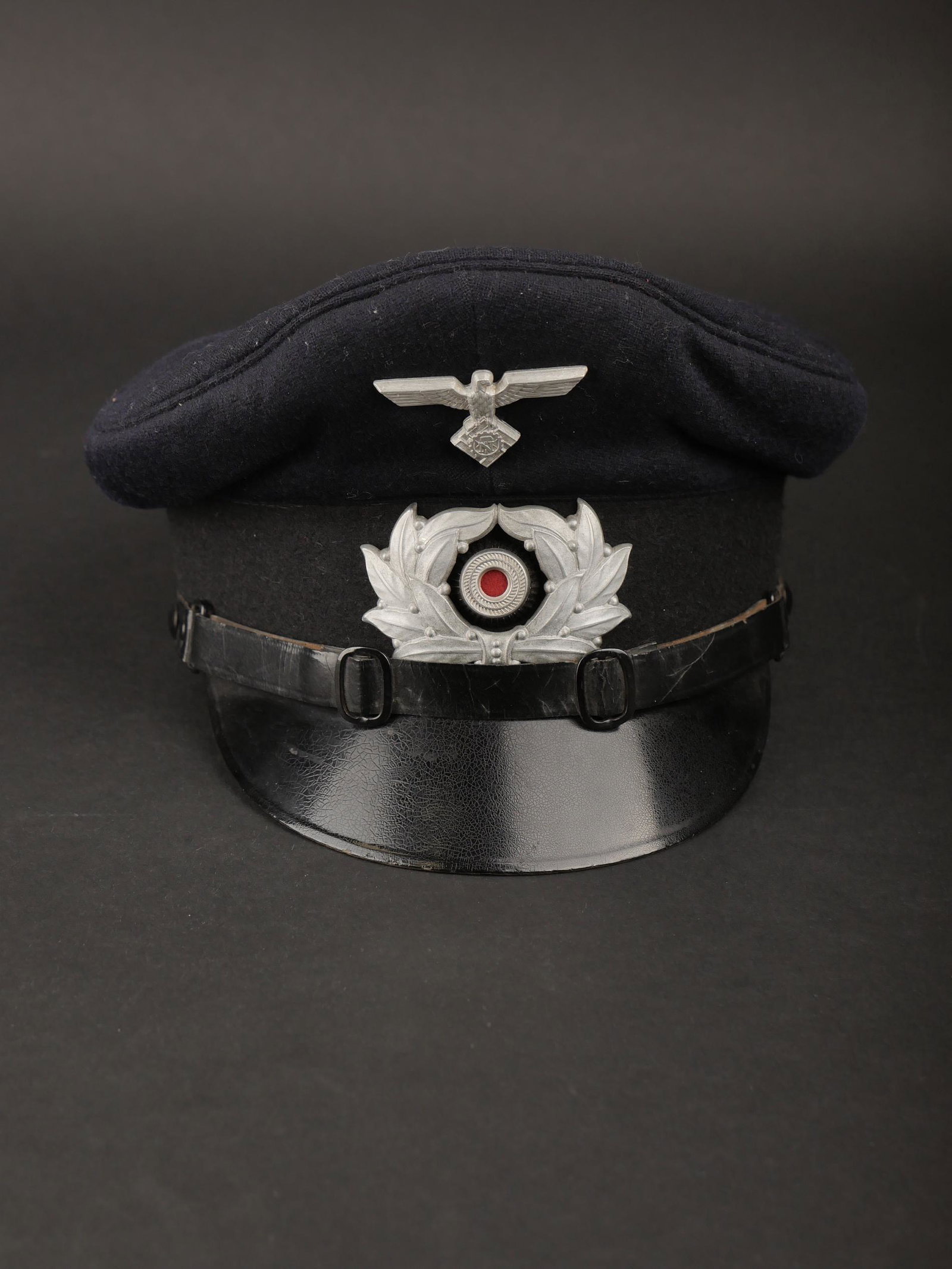 Casquette de sous officier Teno. Teno non commissioned officer s cap.: Casquette de sous officier Teno. En drap noir. Bandeau en velours noir. Insignes metalliques. Les insignes n ont pas ete demontes afin de verifier les attaches. Fausse jugulaire complete. Interieur do
