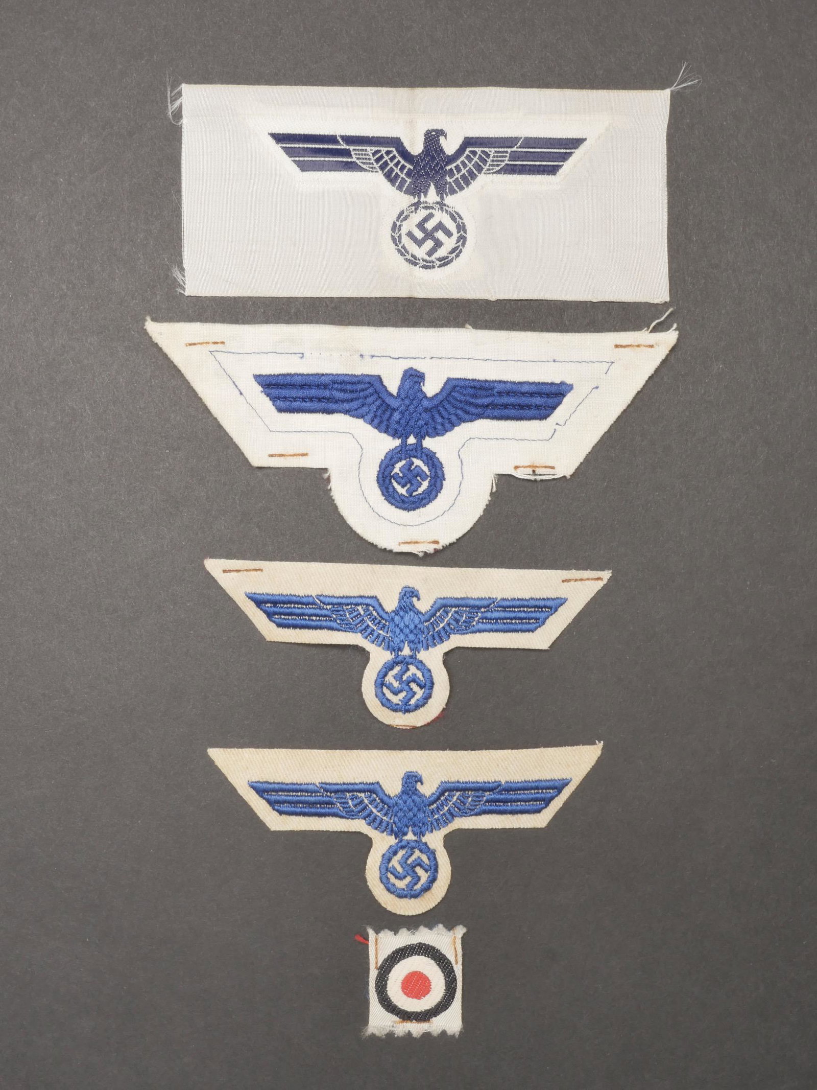 Aigles d uniforme Kriegsmarine. Kriegsmarine uniform eagles.: Aigles d uniforme Kriegsmarine. Comprenant un aigle brode bleu sur fond blanc, jamais monte. Une cocarde tisse sur fond blanc, jamais montee. Un aigle brode bleu sur tissu coton blanc, jamais monte. U
