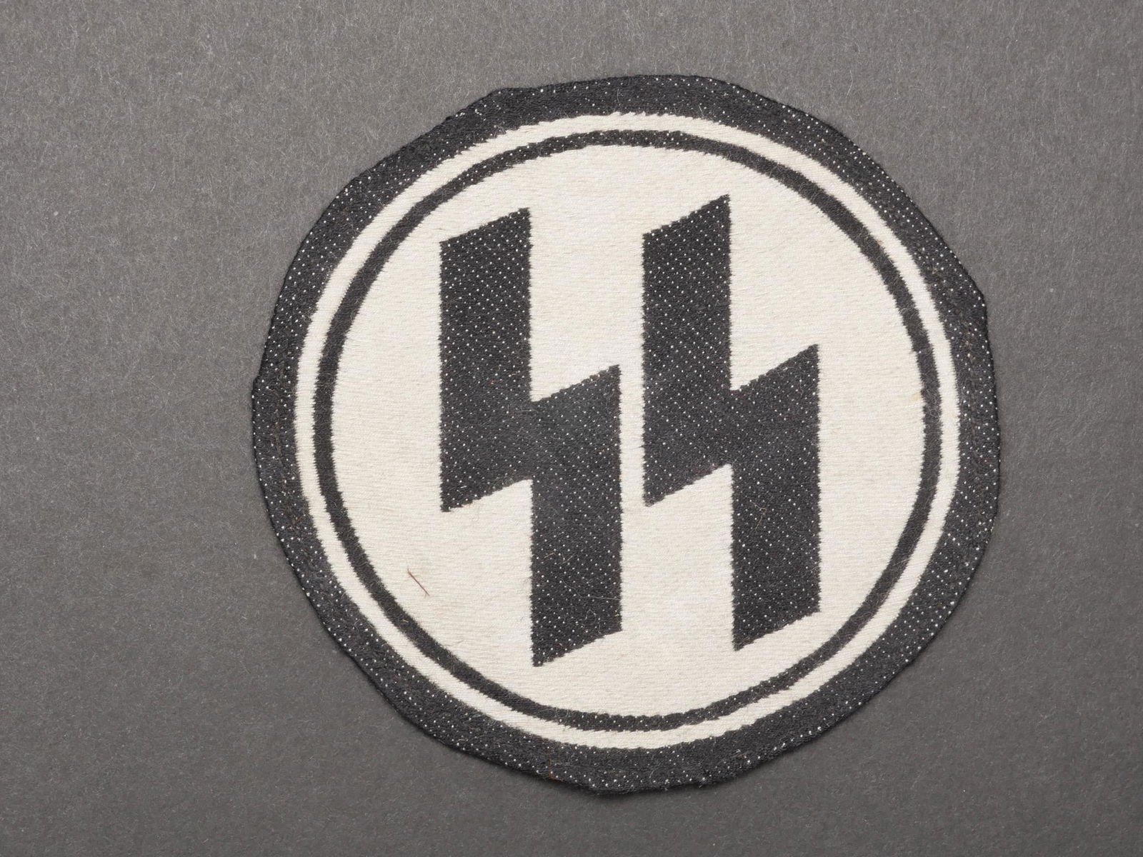 Insigne de maillot de sport SS. SS sports shirt badge.: Insignes de maillots de sport SS. Modele tisse. Plie d origine. Etiquette RZM SS, numero 072710, code fabricant 348. Diametre 10,3 cm. A noter une certaine usure et patine de la piece. Etat II+. SS sp