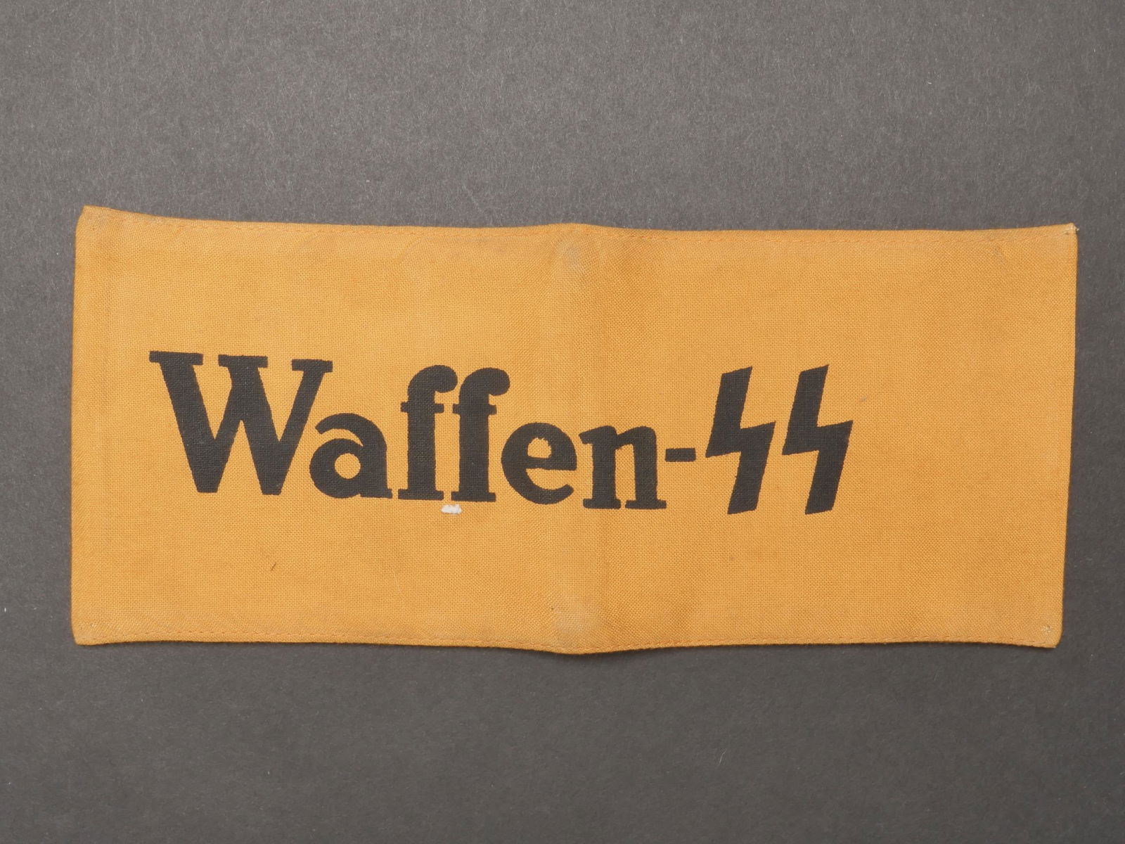 Brassard Waffen SS. SS armband.: Brassard Waffen SS. En tissu coton orange. Marquage imprime Waffen SS. Sans marquages fabricant visibles. A noter une certaine usure et patine de la piece, ainsi que des taches. Etat II+. Waffen SS ar