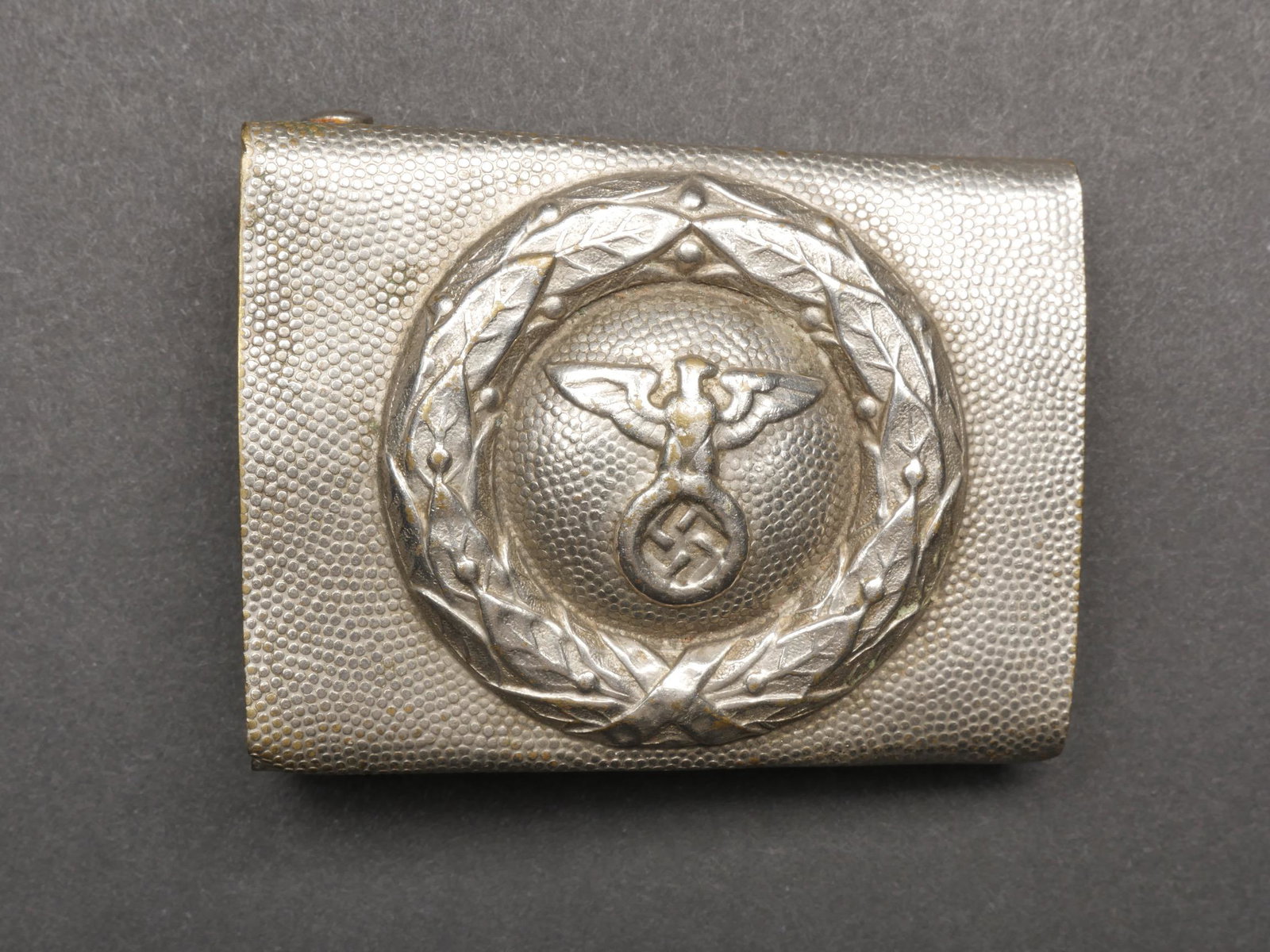 Boucle de ceinturon RSLV. RSLV Belt Buckle.: Boucle de ceinturon RSLV. En aluminium grenele. Fabrication en creux. Boucle a deux ardillons complete. Sans marquages fabricant visible. A noter une certaine usure et patine de la piece. Etat II+. Be