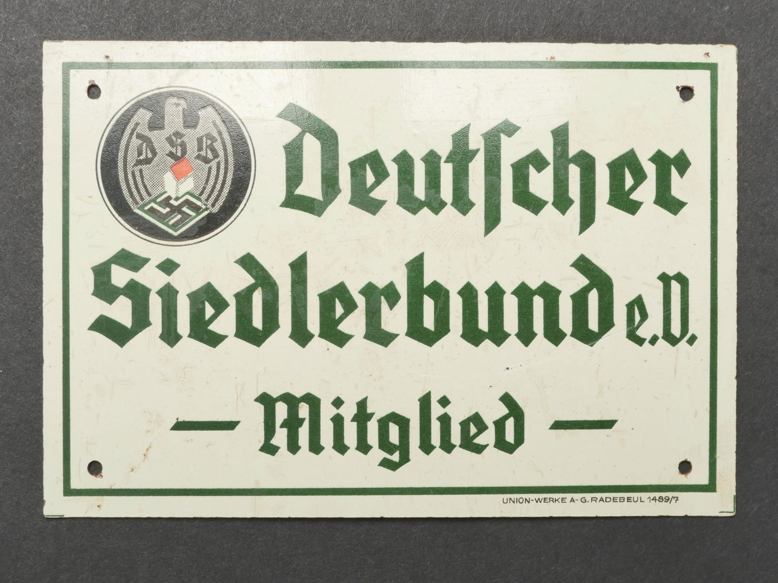 Plaquette DSB. DSB plate.: Plaquette DSB. En bakelite peinte. Quatre points de fixation. Fond blanc et lisere vert. Bel insigne DSV. Marquages Deutscher Siedlerbund eV Mitglied. Fabrication Union Werke A G Radebeul 1489/7. Dime