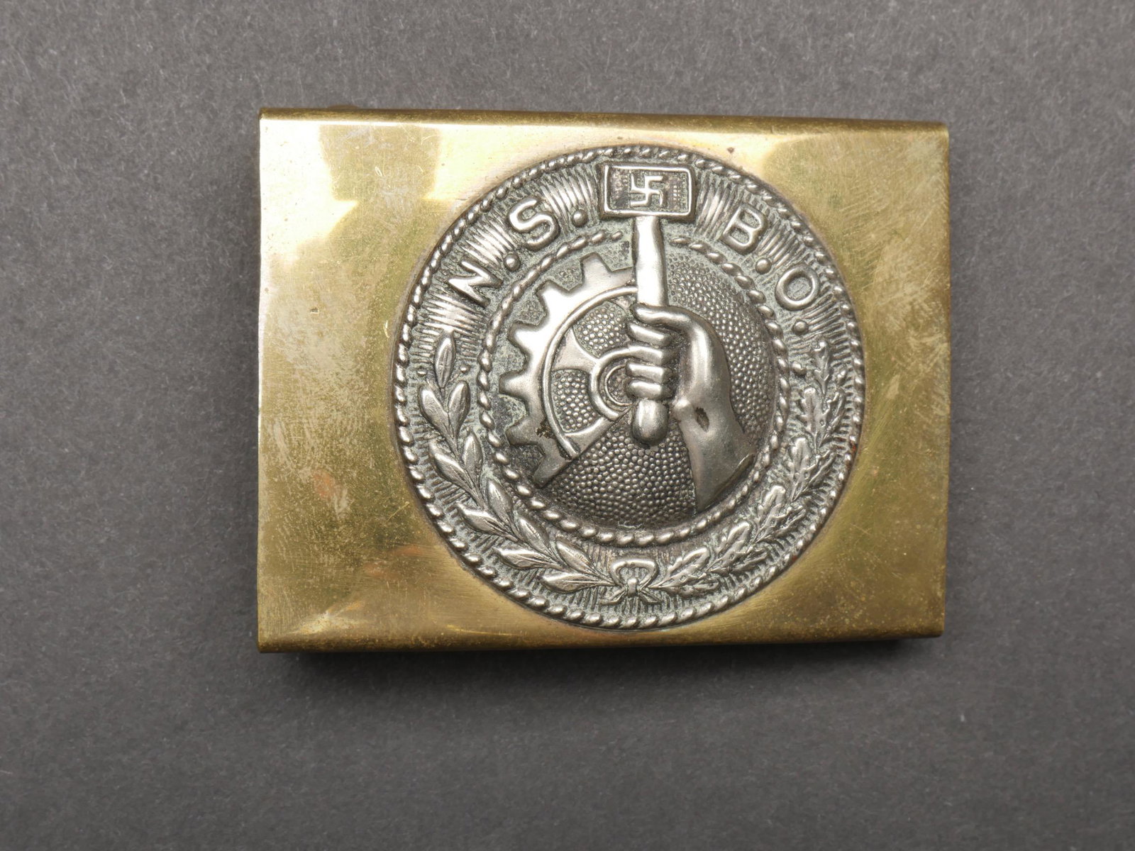 Boucle de ceinturon NSBO. NSBO Belt Buckle.: Boucle de ceinturon NSBO. En metal et laiton. Fabrication en deux parties. Insigne en relief. Boucle a deux ardillons presente. Sans marquage fabricant visible. Un point de soudure manquant. A noter u