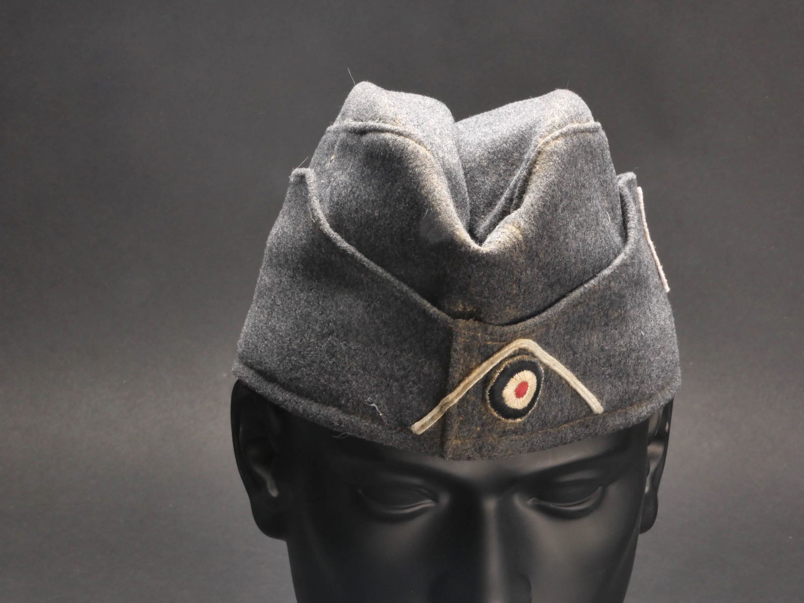 Calot DRK. DRK cap.: Calot DRK. En drap gris. Insigne tisse cousu machine cote gauche du calot. Cocarde brodee visiblement montee d origine. Soutache blanche. Interieur double en tissu coton gris. Tampon indiquant une tai