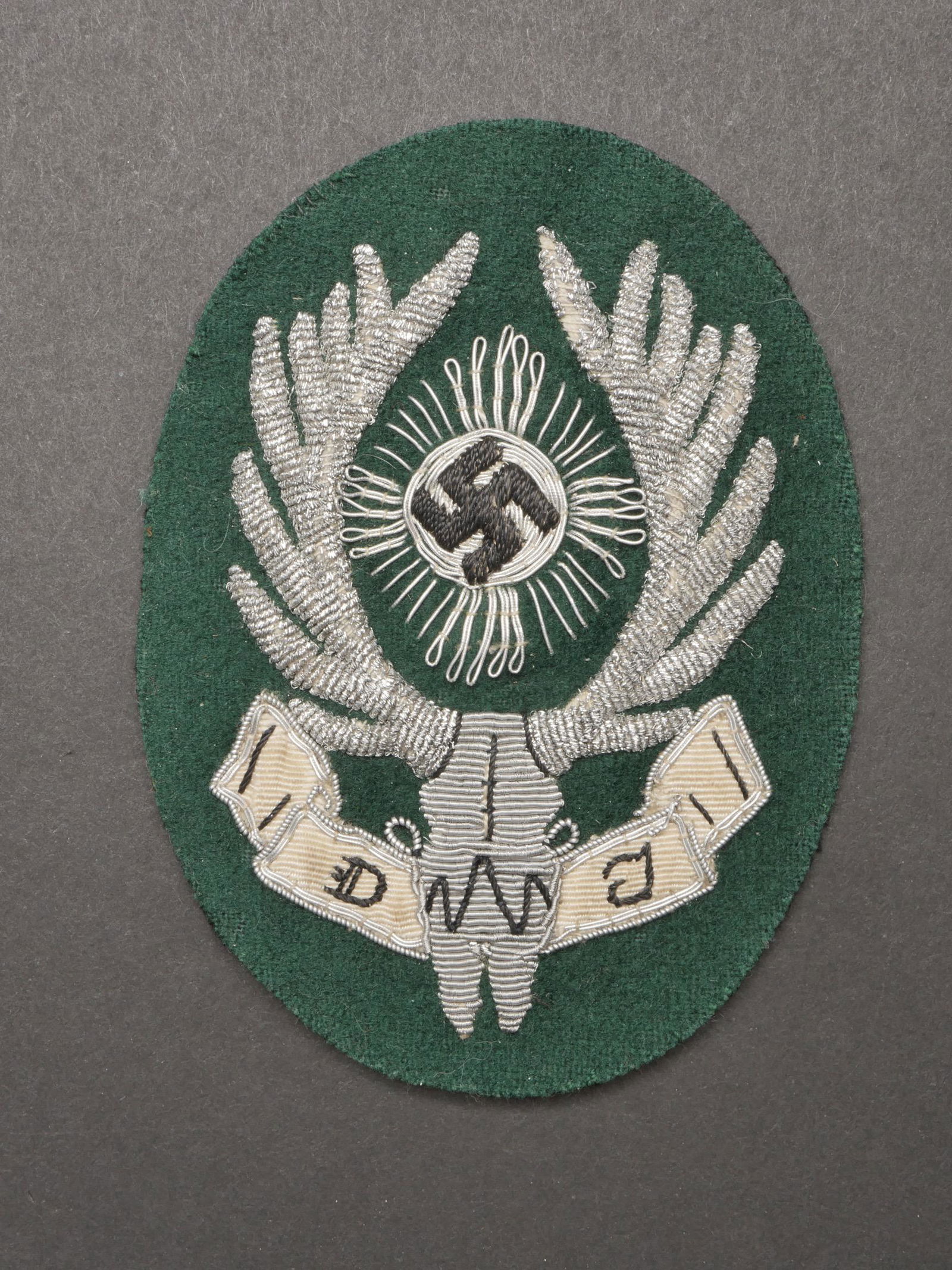 Insigne de manche DJ. DJ sleeve badge.: Insigne de manche DJ. En cannetille argent sur fond vert foret. Dos de la piece double de tissu noir. A noter une certaine usure et patine de la piece. Etat II+. Badge of sleeve DJ. In silver cannetil