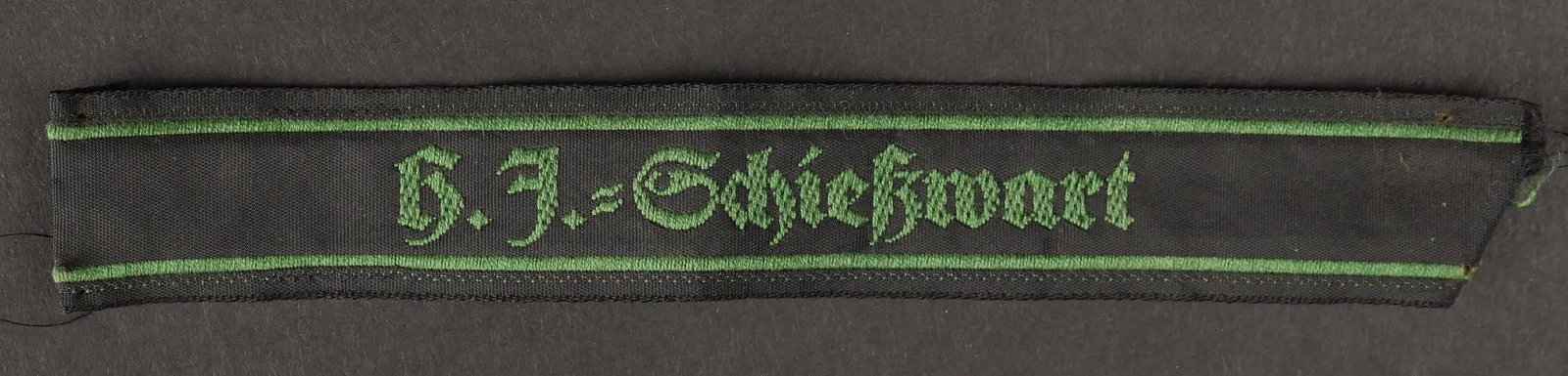 HJ Schiesswart. Hj Schiesswart.: Hitlerjugend Schiesswart. En tissu noir, tissage en fil vert, marque HJ Schiesswart. Longueur 14 cm. Jamais monte. A noter une legere usure et patine de la piece. Etat I-. Hitlerjugend Schiesswart. In