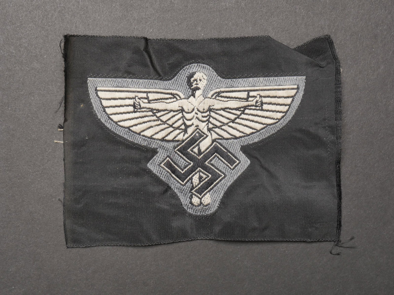 Insigne NSFK. NSFK insignia.: Insigne NSFK. Modele tisse sur fond noir. Jamais monte. Traces de colle au dos. A noter une legere usure et patine de la piece. Etat I-. NSFK badge. Woven pattern on black background. Never mounted. T