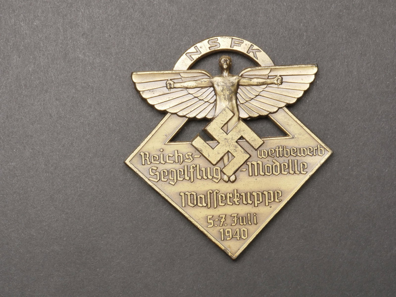 Plaquette NSFK. NSFK Plate.: Plaquette NSFK. En metal, couleur doree a 70%. Bel insigne NSFK en relief. Marquages Reichswettbewerb Segelflug Modelle Wasserkuppe 5-7 juli 1940, traces de colle au dos. Dimensions 8 x 7,5 cm. A note