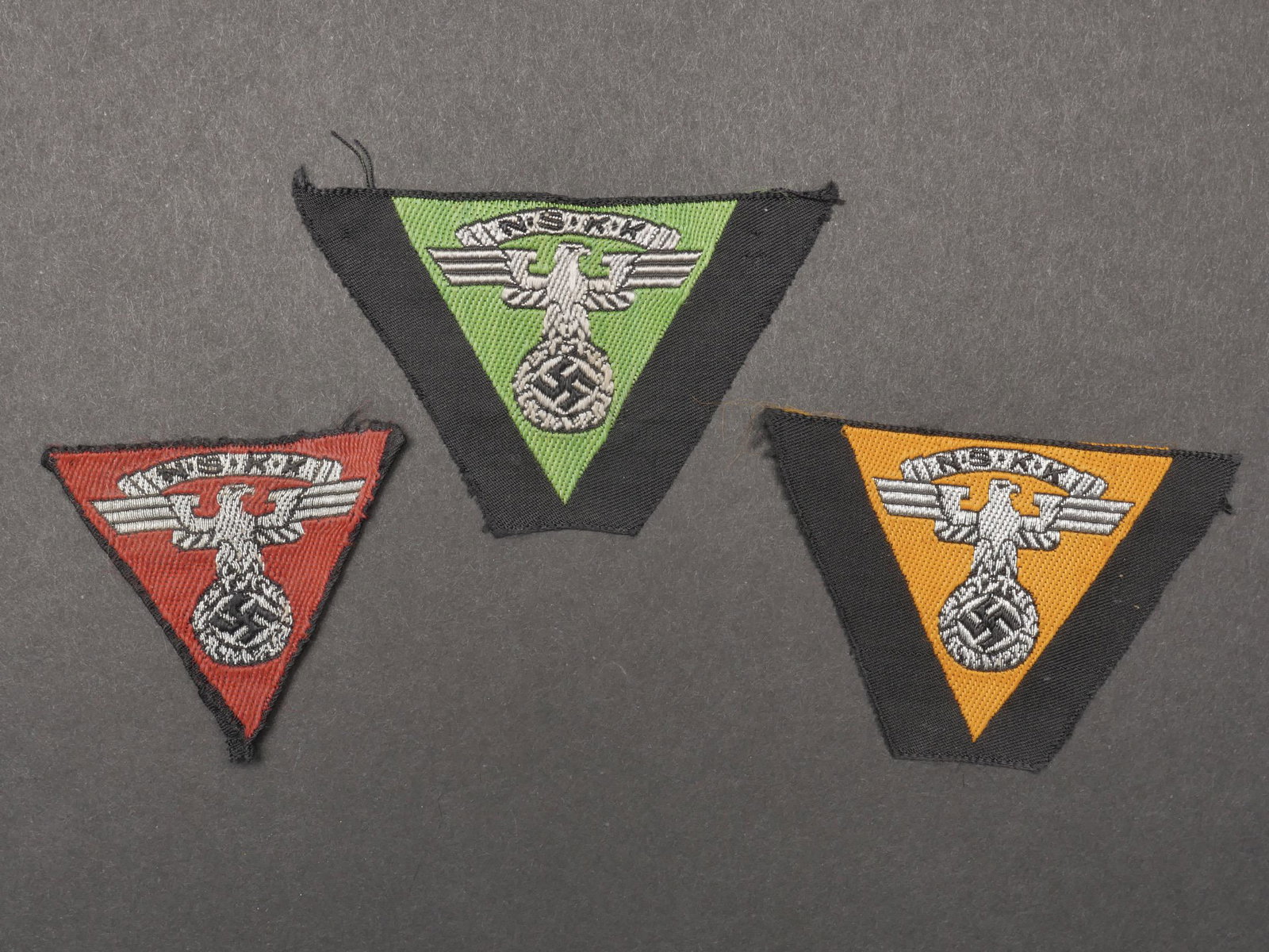 Insignes de calot NSKK. NSKK cap badges.: Insignes de calot NSKK. Comprenant un aigle tisse jamais monte, sur fond jaune pour le M Gruppe Niederschlesien. Un insigne de calot jamais monte, sur fond vert pomme pour le M Gruppe Ostsee. Un insig