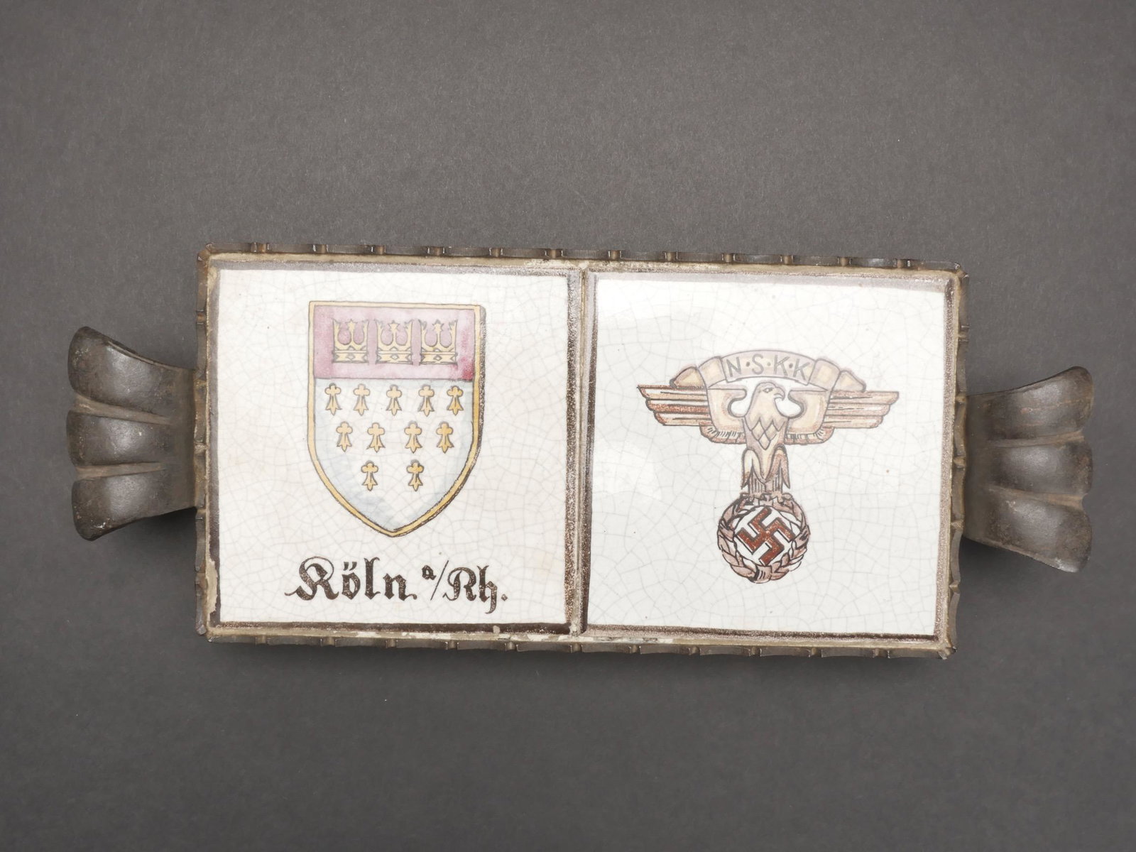 Plateau NSKK. NSKK deck.: Plateau commemoratif NSKK. Support en metal disposant de quatre pieds. Deux carreaux en faiences craquelee. Le premier carreau represente les armes de la ville de Koln am Rhein. Le second represente l