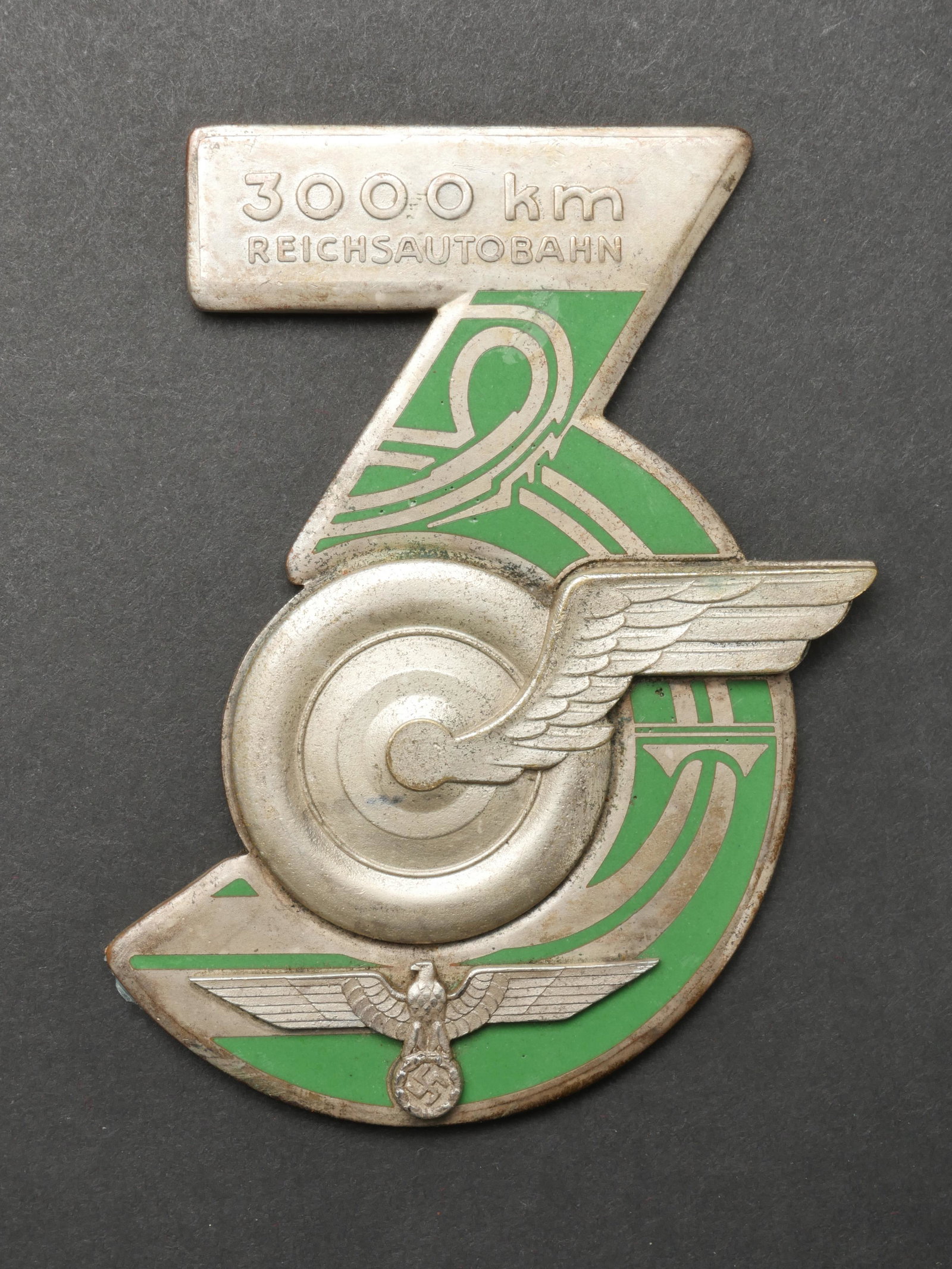 Plaquette Reichsautobahn. Reichsautobahn plate.: Plaquette Reichsautobahn. En metal couleur argent, et metal emaille. Beaux insignes en relief. Marquages Reichsautobahn 3000 km. Traces de colle au dos. Dimensions 9 x 10 cm. Marquages au dos 15 12 19