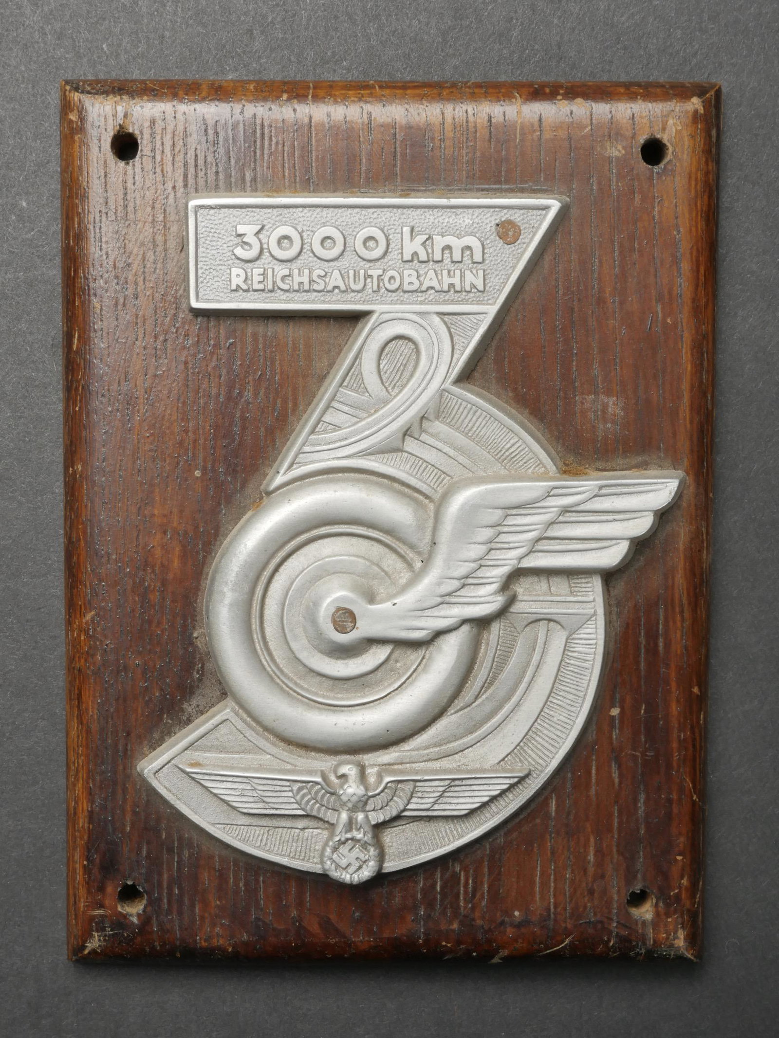 Plaquette Reichsautobahn. Reichsautobahn plate.: Plaquette Reichsautobahn. En metal couleur argent, et metal emaille. Beaux insignes en relief. Marquages Reichsautobahn 3000 km. Monte sur une plaque en bois, quatre points de fixation. Dimensions 10 