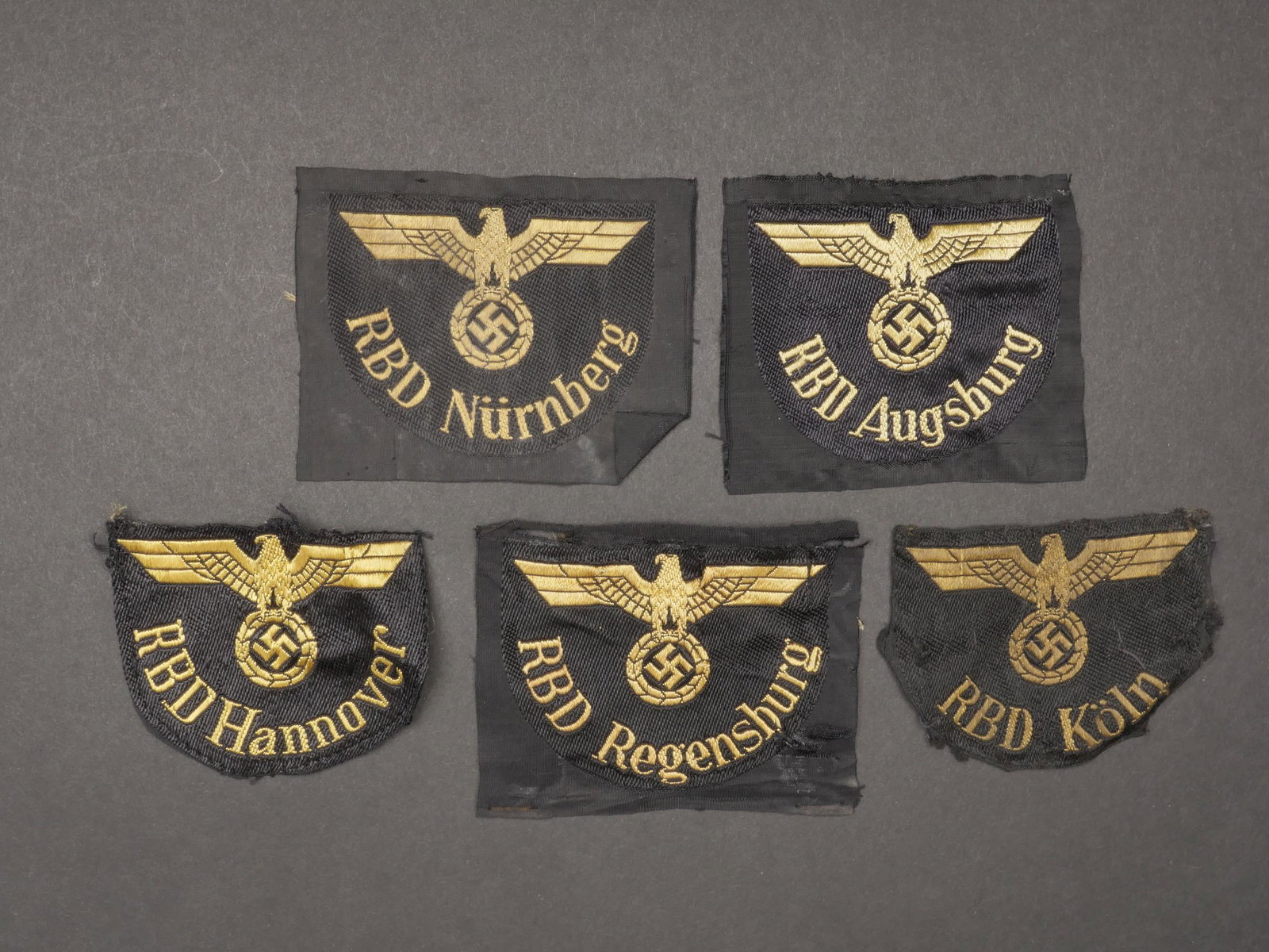Insignes Reichsbahn. Badges Reichsbahn. Armband Zug Begleitung.: Insignes Reichsbahn. Comprenant un insigne de manche tisse RBD Hannover, visiblement demonte d une vareuse. Un insigne tisse RBD Regensburg, jamais monte. Un insigne tisse RBD Augsburg, jamais monte. 