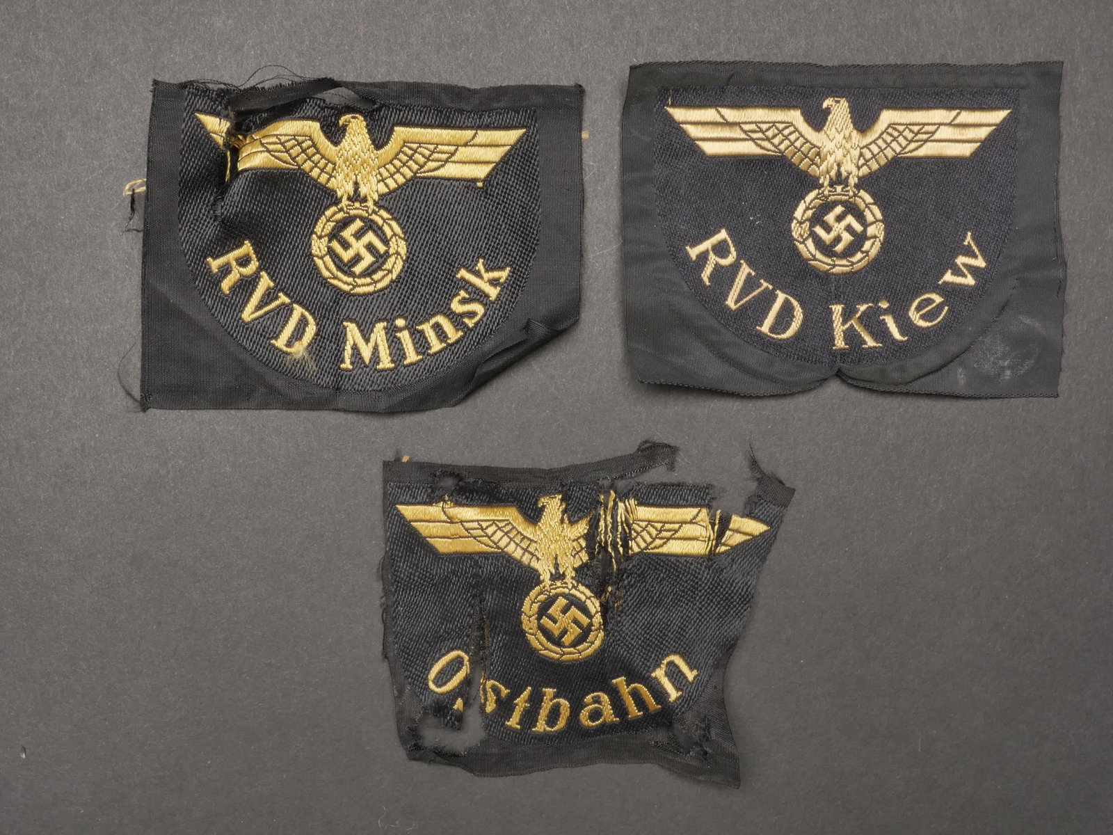 Insignes Reichsbahn. Insignia Reichsbahn.: Insignes Reichsbahn. Comprenant un insigne de manche tisse Ostbahn, dechire, jamais monte. Un insigne tisse RBD Kiew, jamais monte. Un insigne tisse RBD Minsk, dechire, jamais monte. A noter une certa