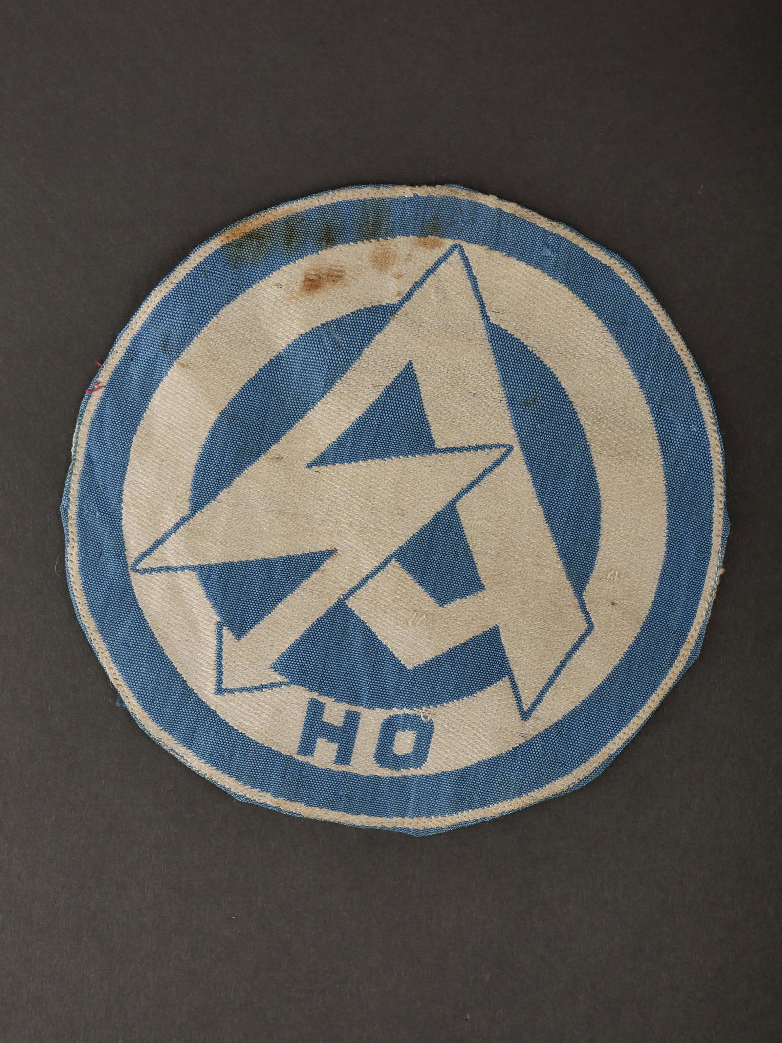 Insigne SA. SA insignia.: Insigne de maillot de sport SA. Modele tisse sur fond blanc, logo SA en tisse en fils bleu ciel, lettrage HO. Jamais monte. Sans marquages visibles. Diametre 14,5 cm. Etiquette RZM absente. A noter un
